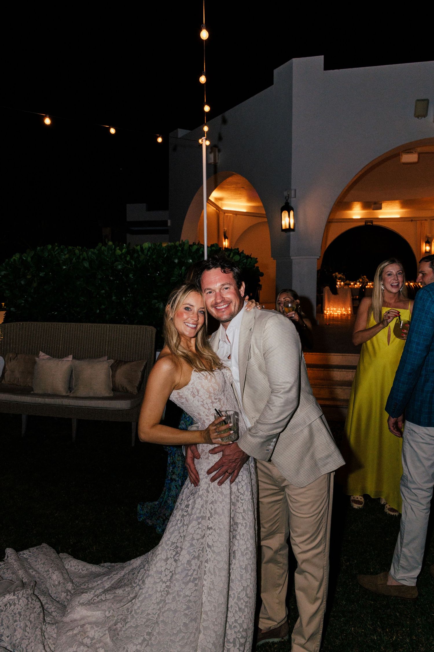 Couples dancing at a wedding reception under warm outdoor lighting and string lights.