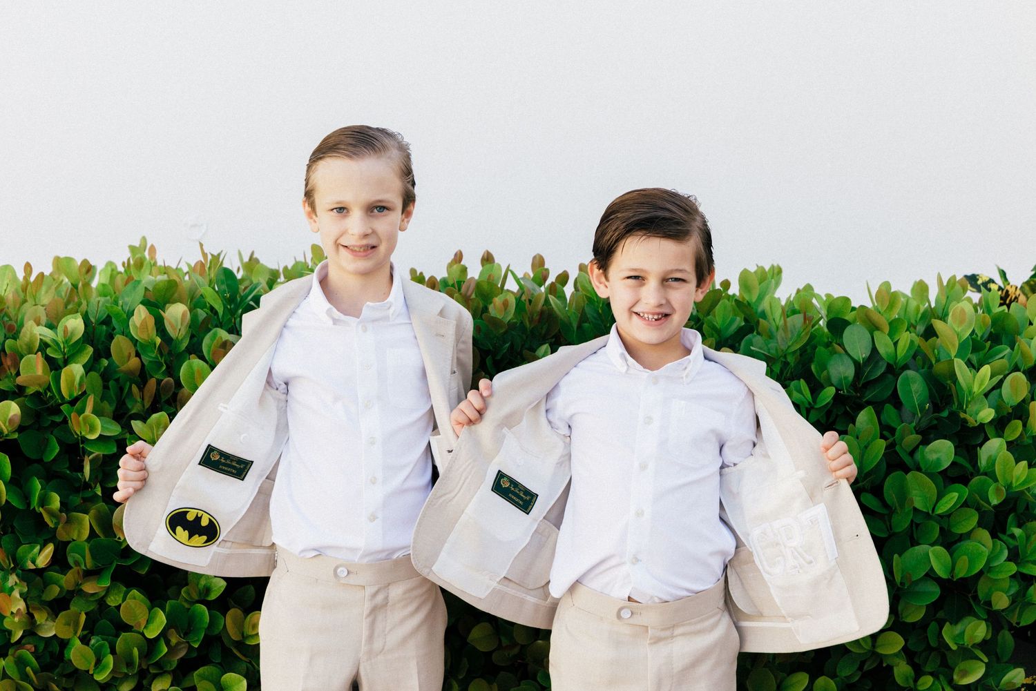 Group wearing matching beige suits posing against a green hedge backdrop.