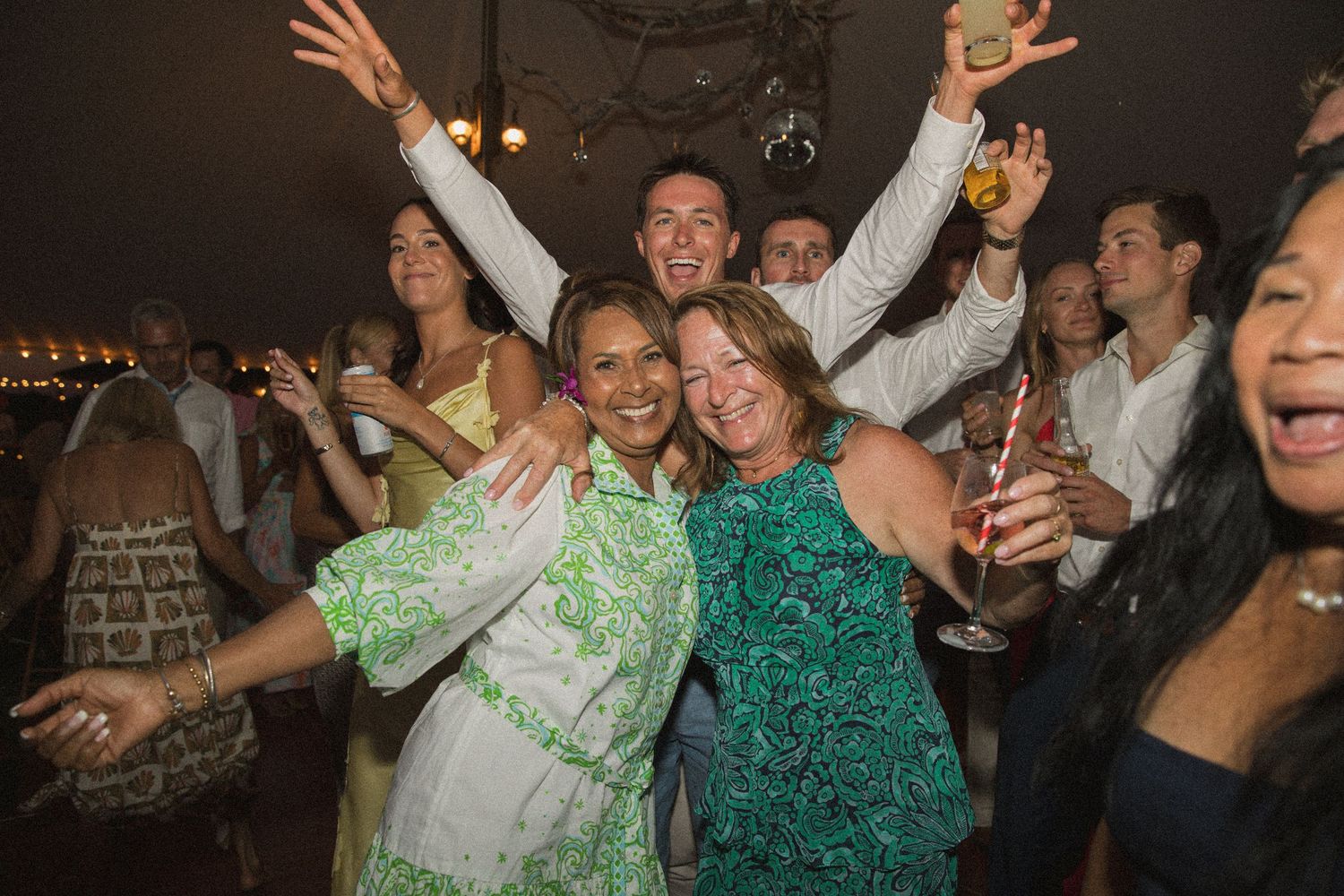 Energetic crowd dancing and celebrating at a nighttime wedding reception.
