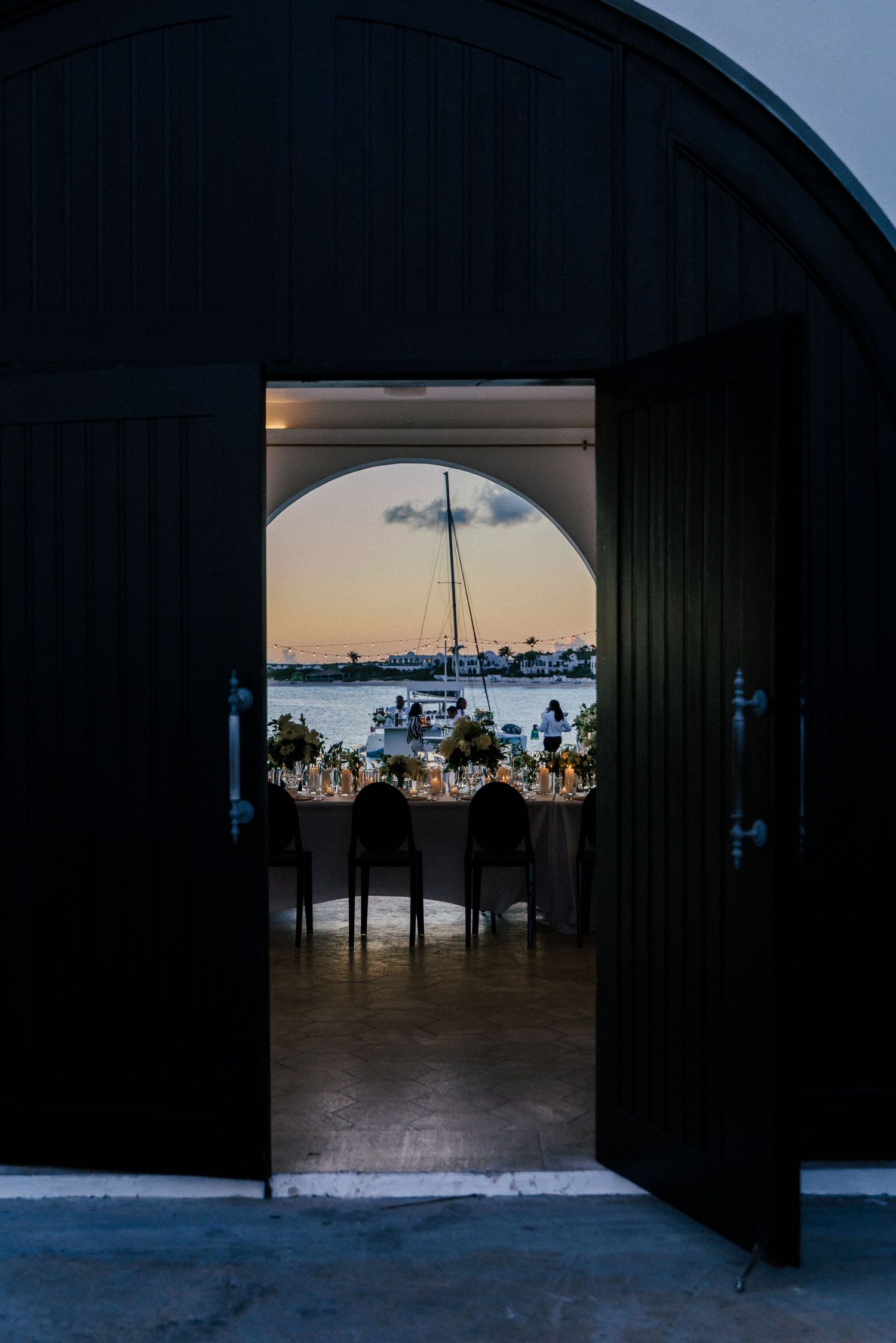 Arched doorway frames elegant wedding reception setup with ocean view.