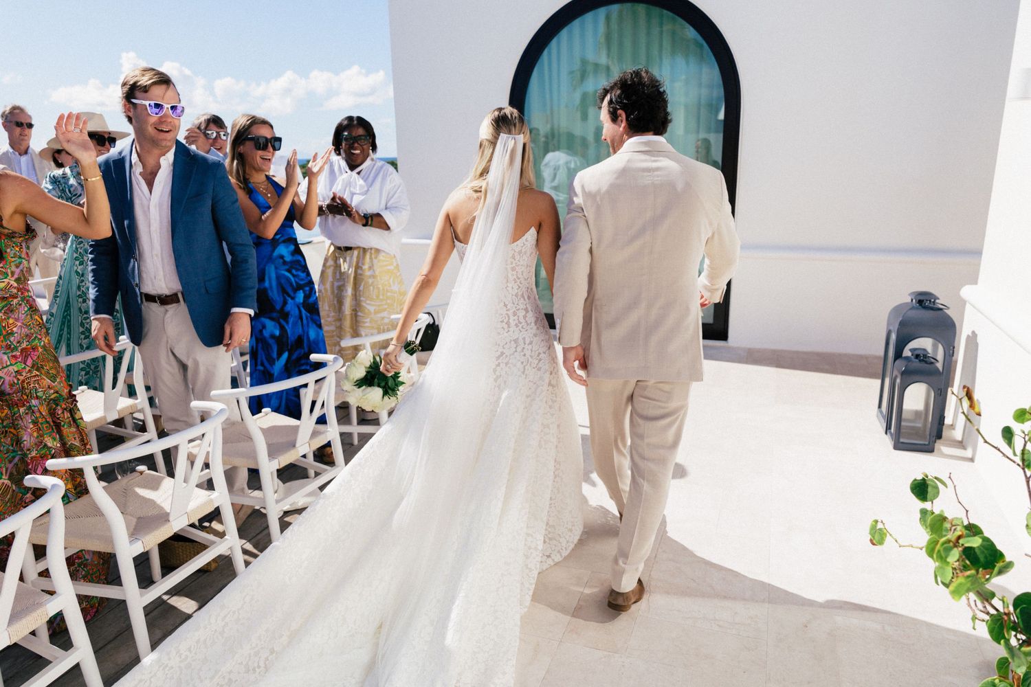 Wedding party walking through a white Mediterranean-style venue with arched doorways and elegant decor.