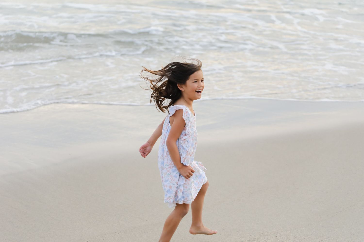 Children running and playing along the shoreline of a sandy beach at sunset.