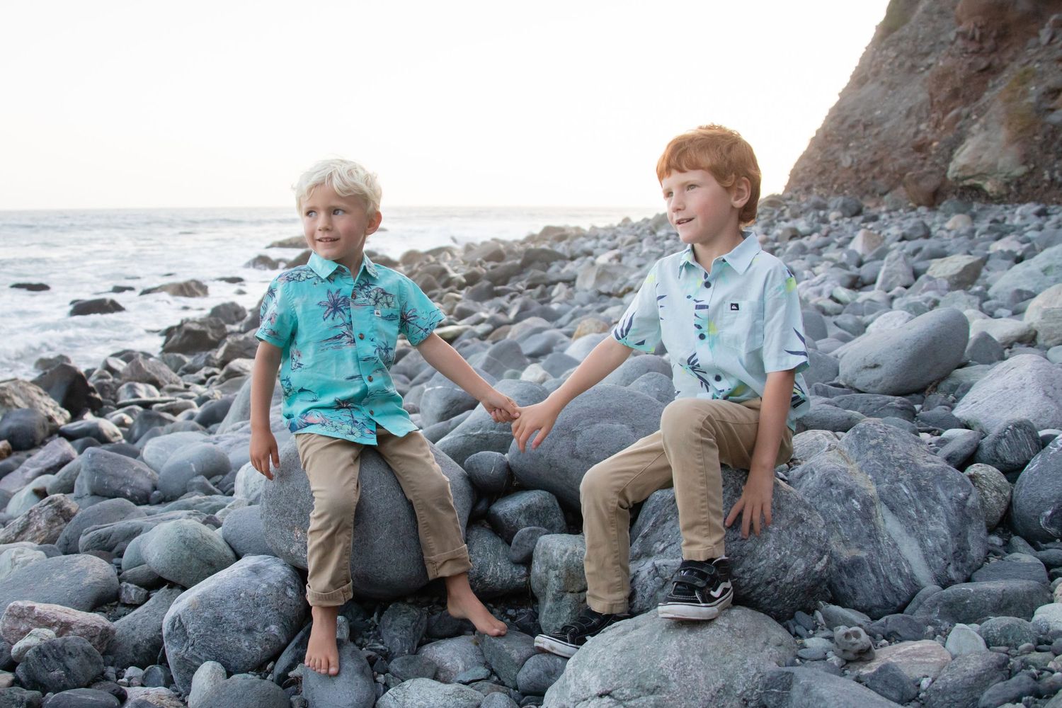 Kids playing on dark rocky beach with coastal cliffs behind them.