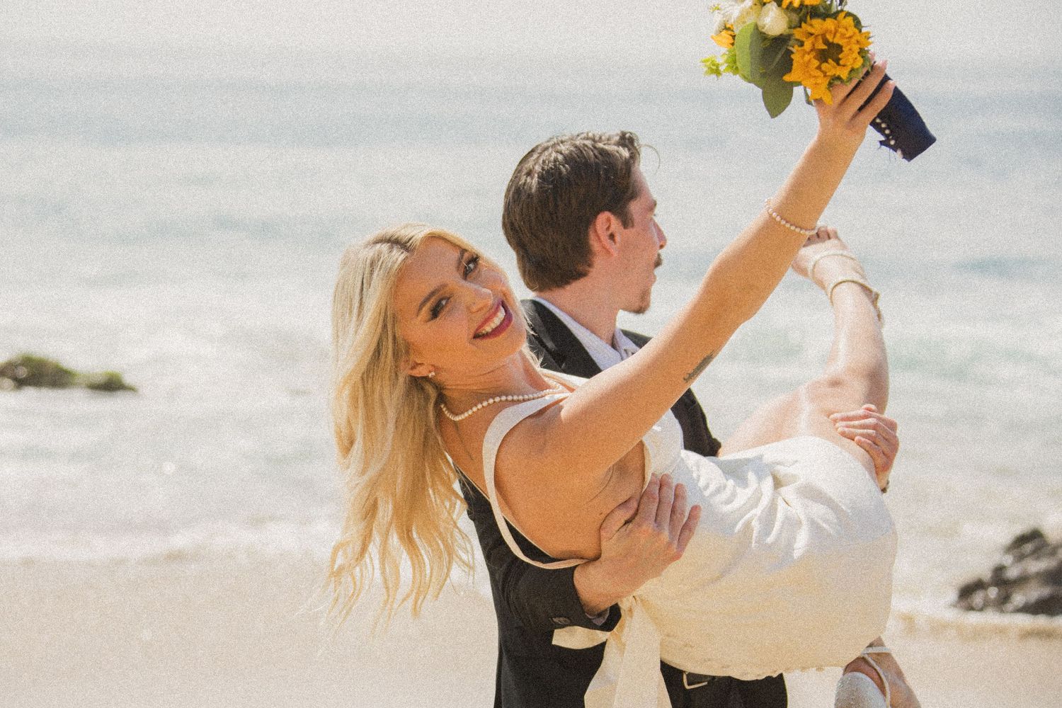 Wedding couple shares energetic dance moves on beach with waves in background.