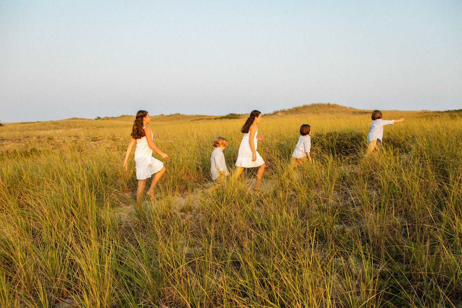 People walking through tall grass on coastal dunes at sunset.