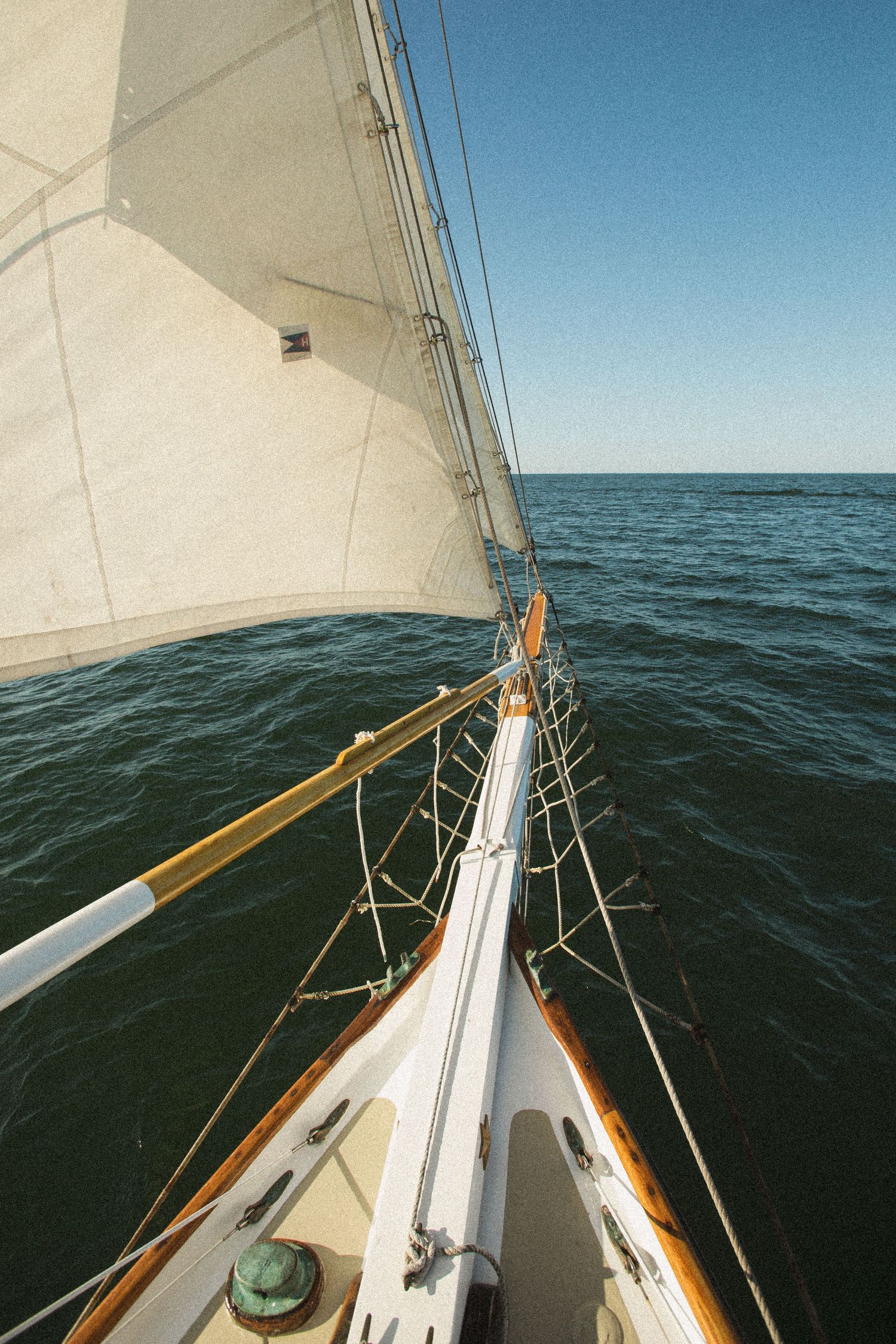Bow view of a classic sailboat with white sails cutting through dark ocean waters.