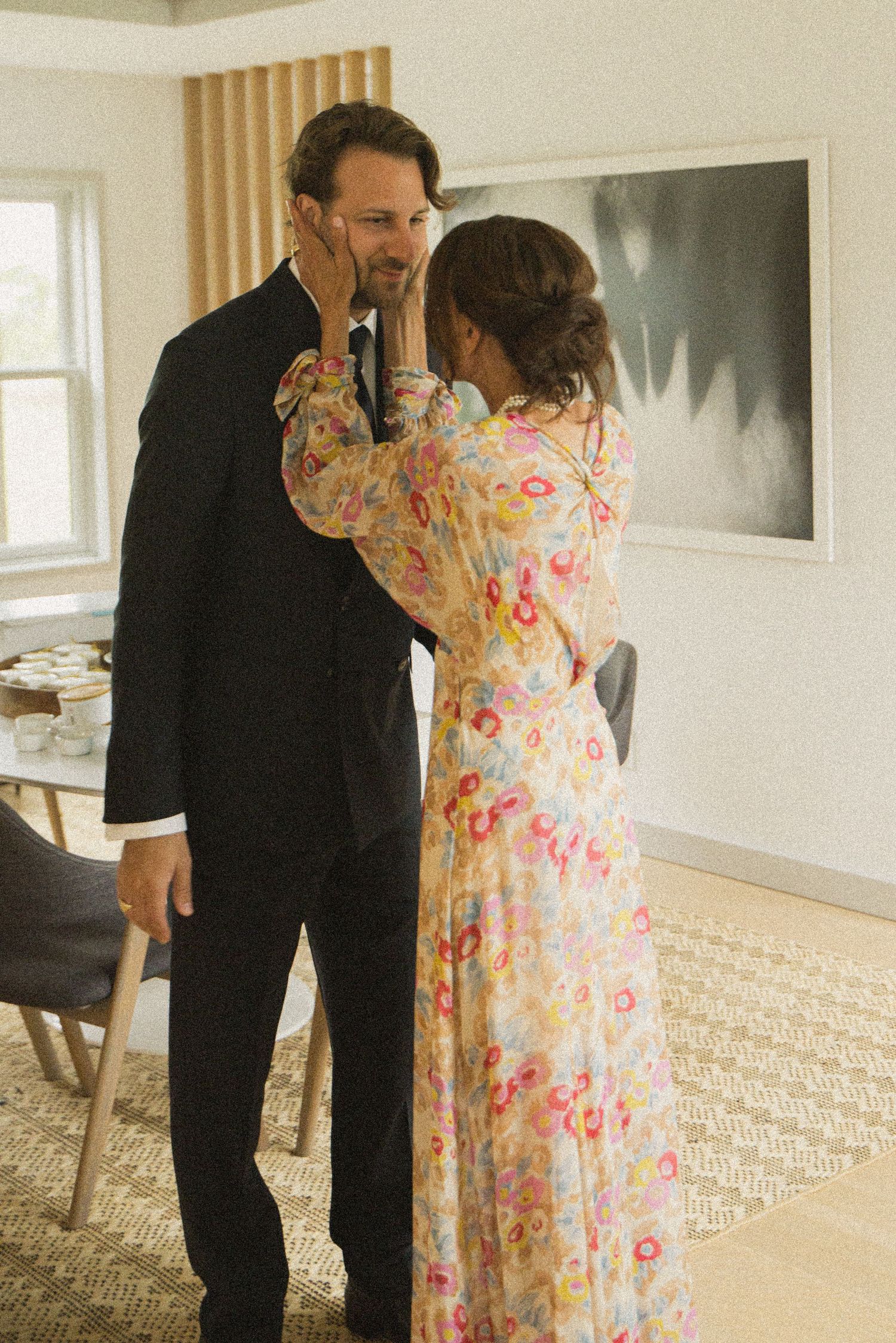 Couple sharing a tender moment, woman in floral dress touching man's face in elegant modern interior.