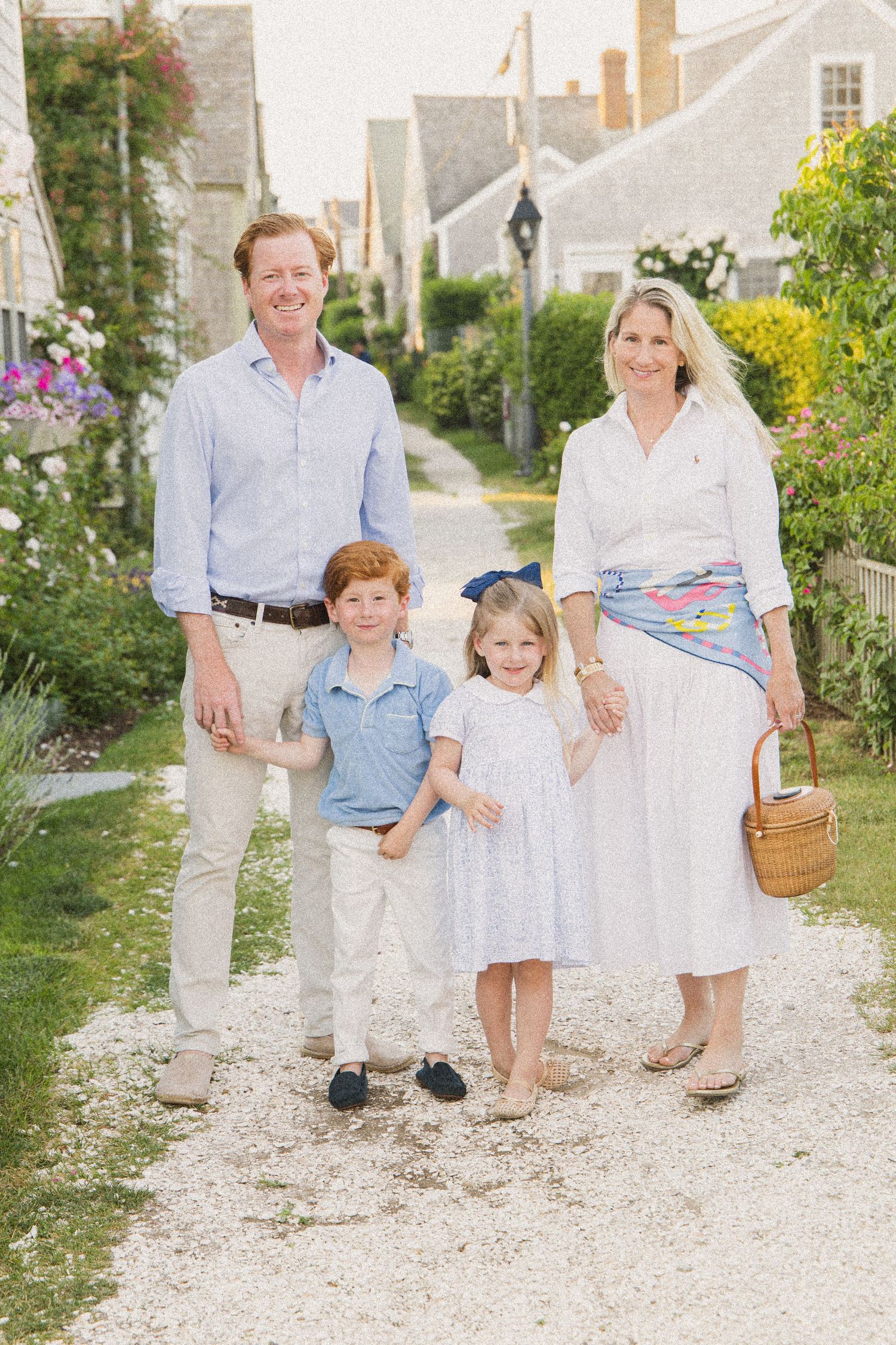 A cheerful family of four poses on a charming garden path in a quaint New England village on a sunny day.