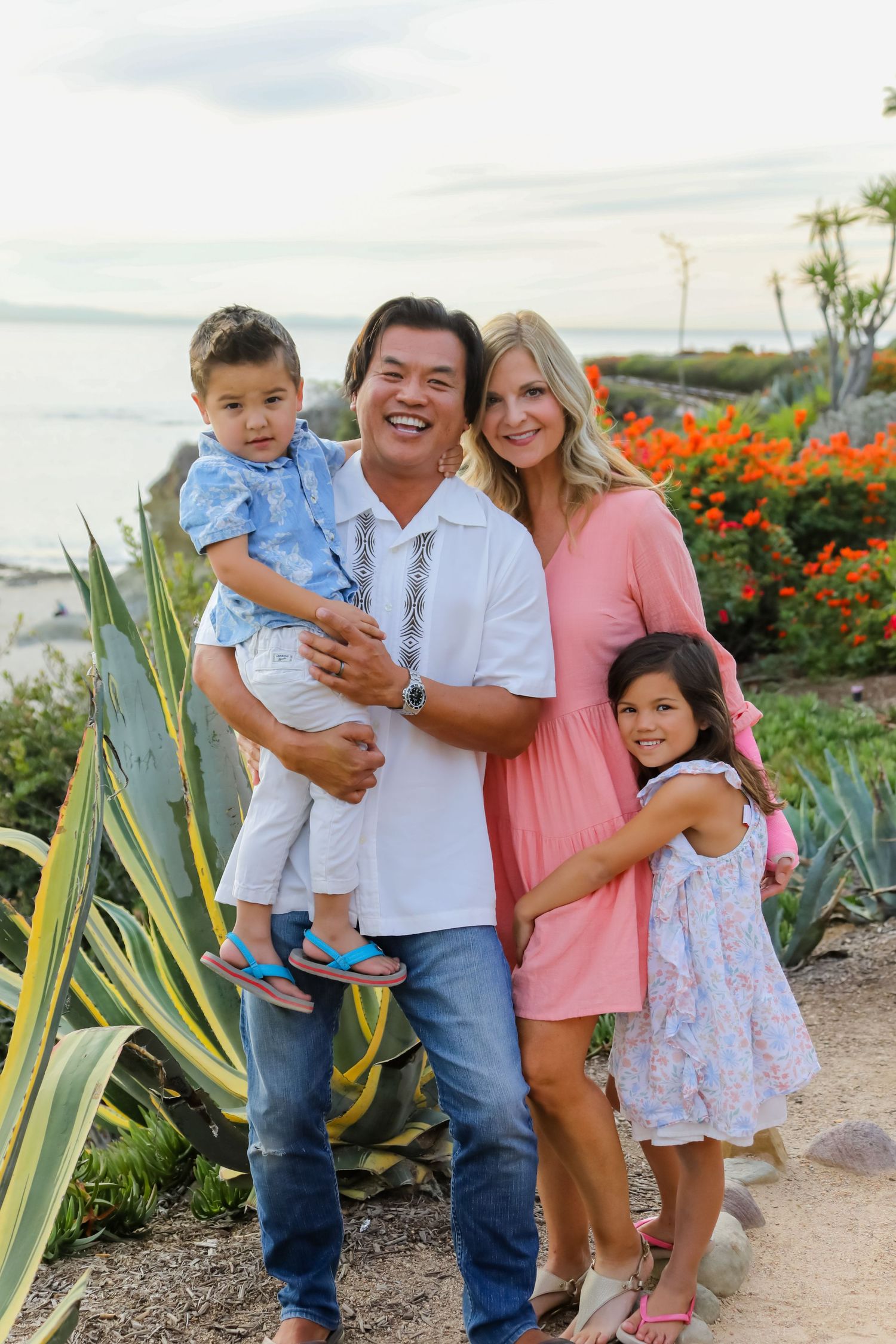 A family poses together on a coastal path with bright orange flowers and ocean views.