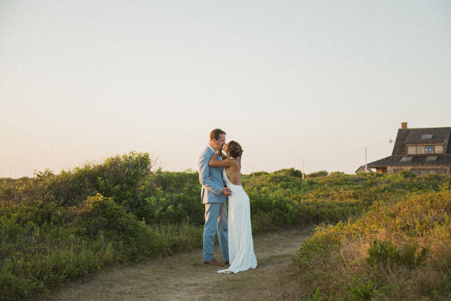 A romantic seaside photoshoot with a couple walking through natural coastal vegetation.