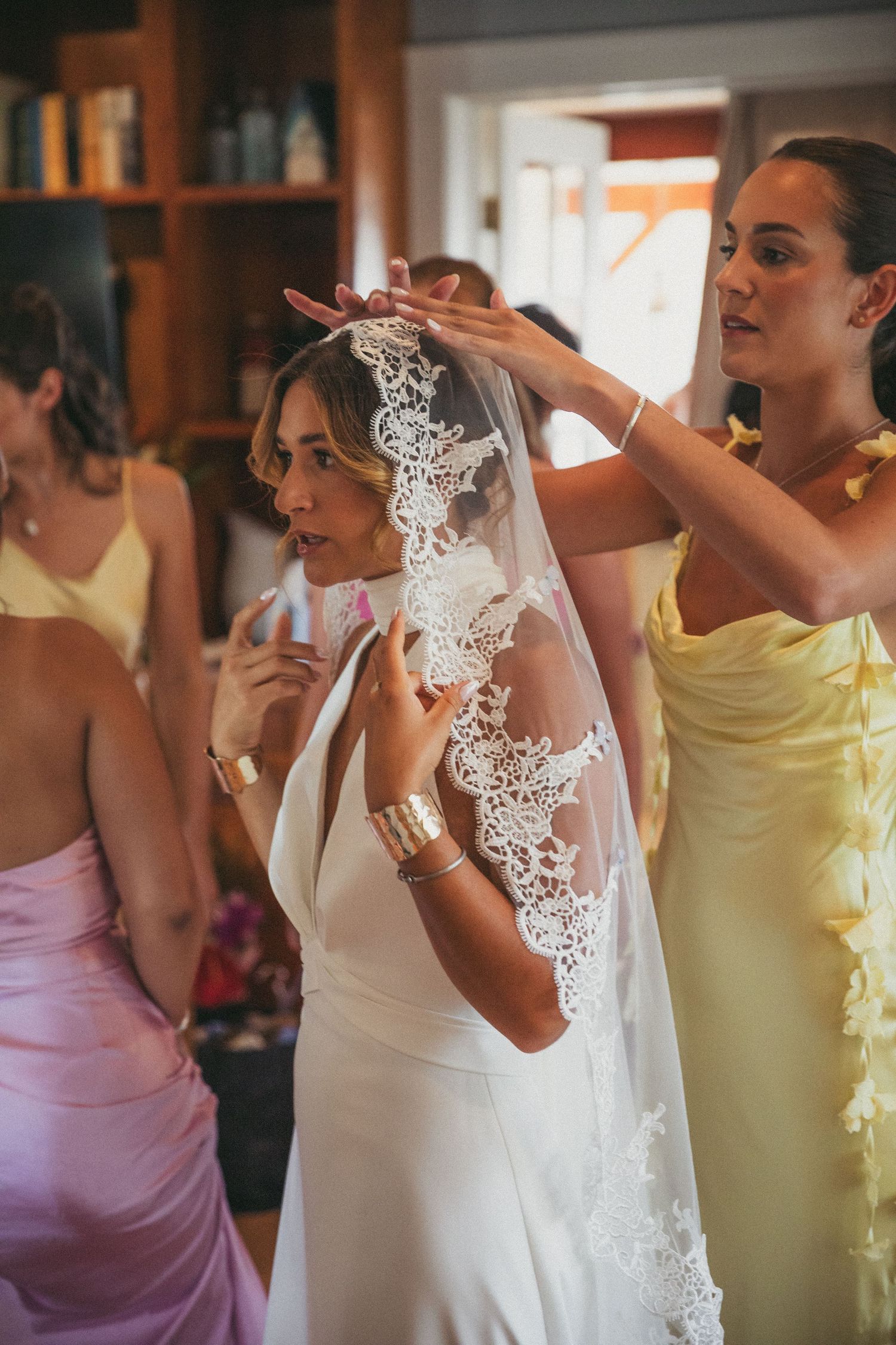 Wedding preparations showing bridesmaids in pastel dresses helping with a lace veil.