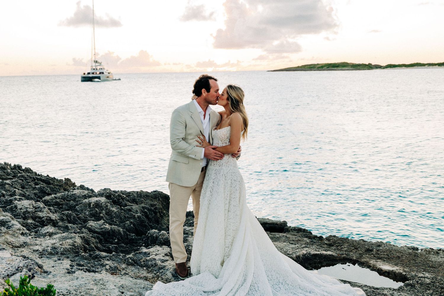 Romantic sunset photos of newlyweds on oceanfront with boats in distance.