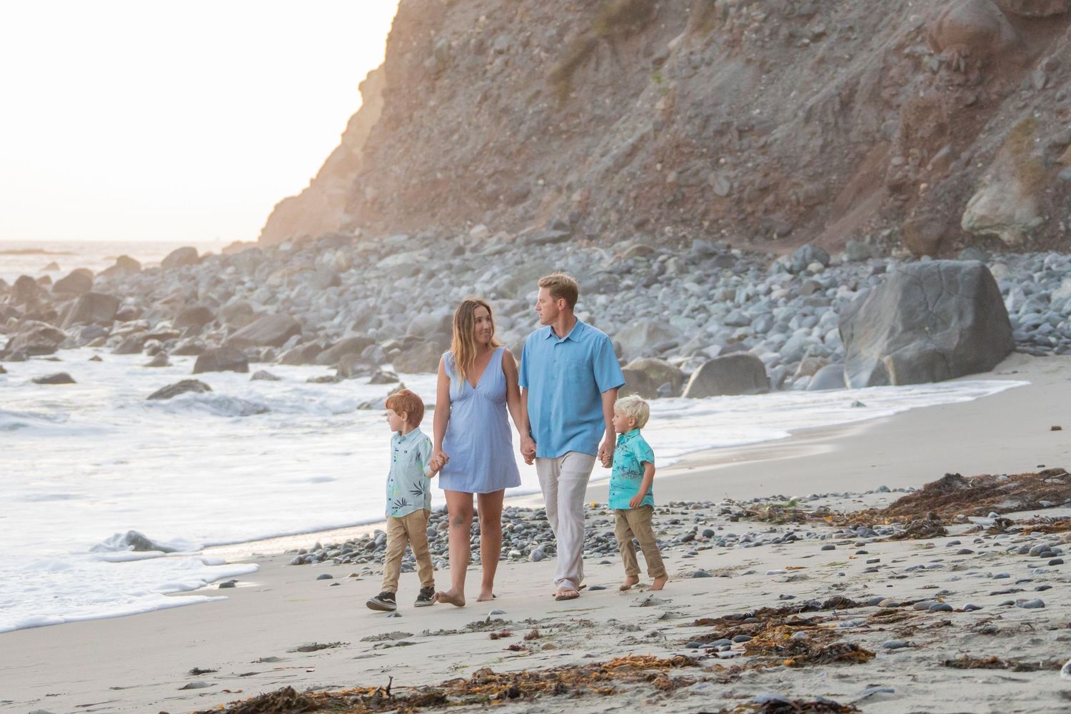Group walking along a scenic beach with rocky cliffs and ocean waves.