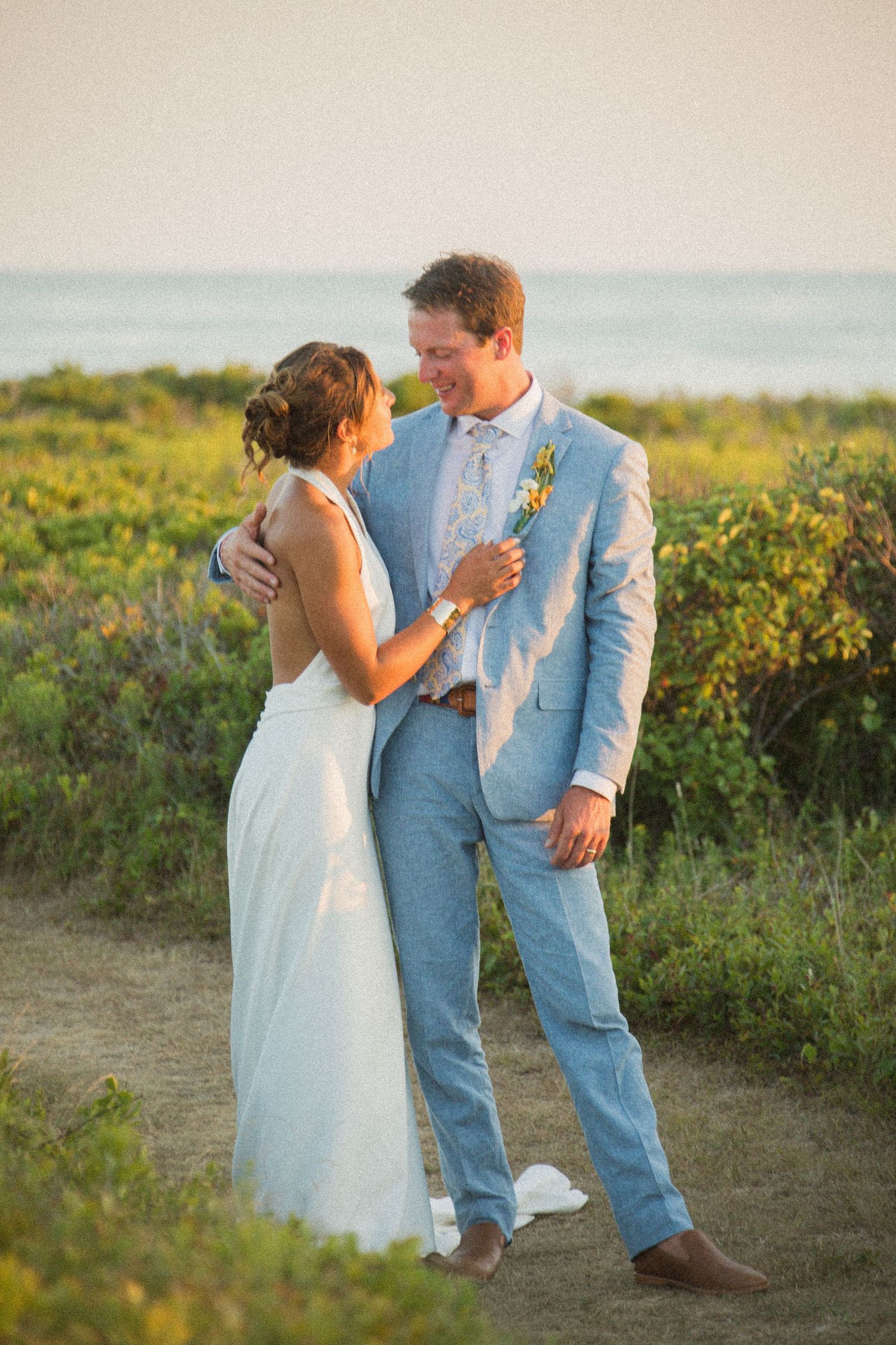 A couple shares an intimate moment on a grassy hillside overlooking the ocean at golden hour.