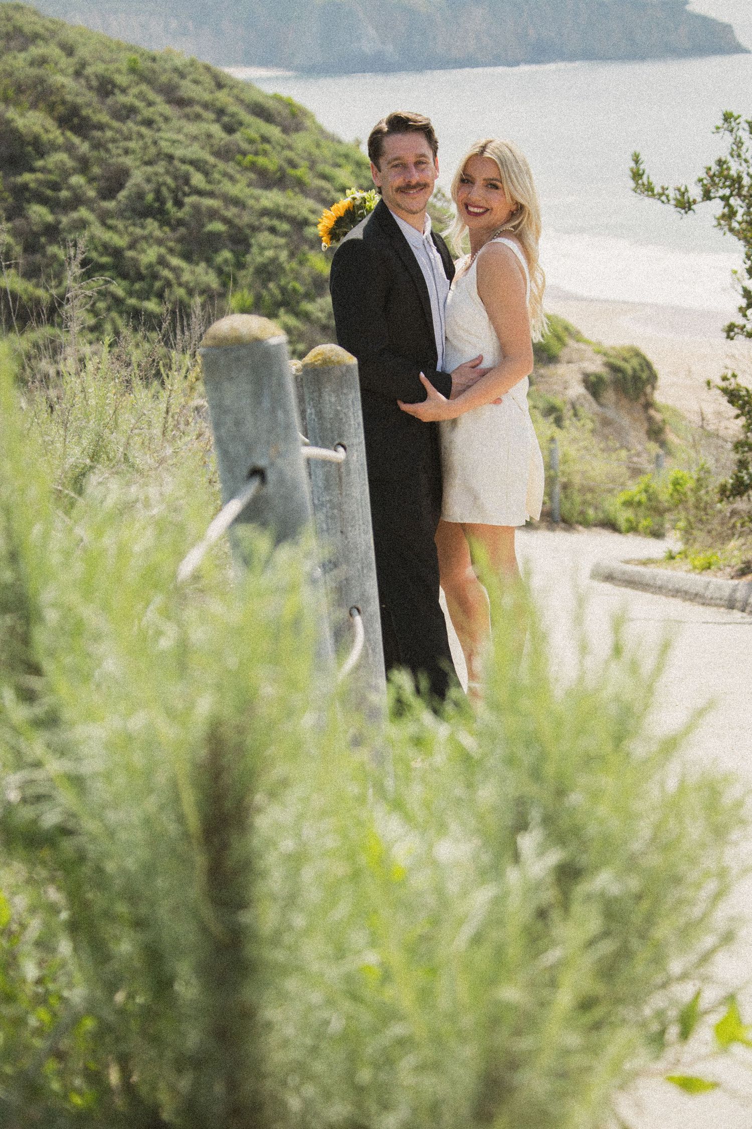 Romantic coastal wedding photoshoot with couple embracing against ocean backdrop.