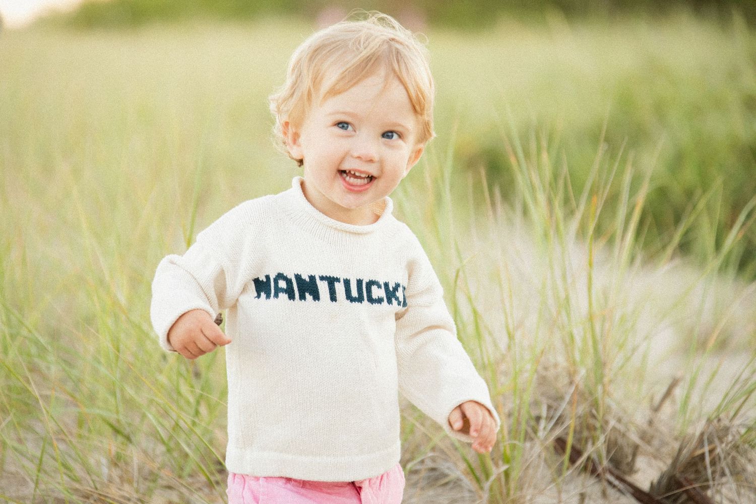 Candid outdoor photography of young children in white clothing on grassy terrain.