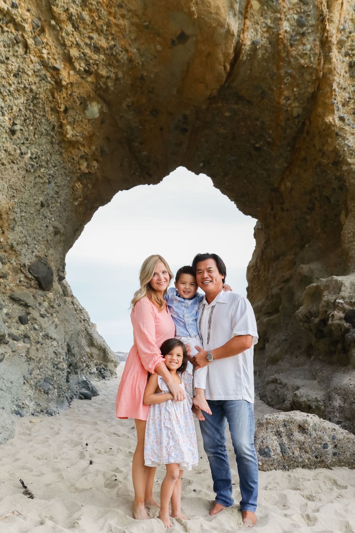 Family sharing tender moment together under natural rock arch at beach.