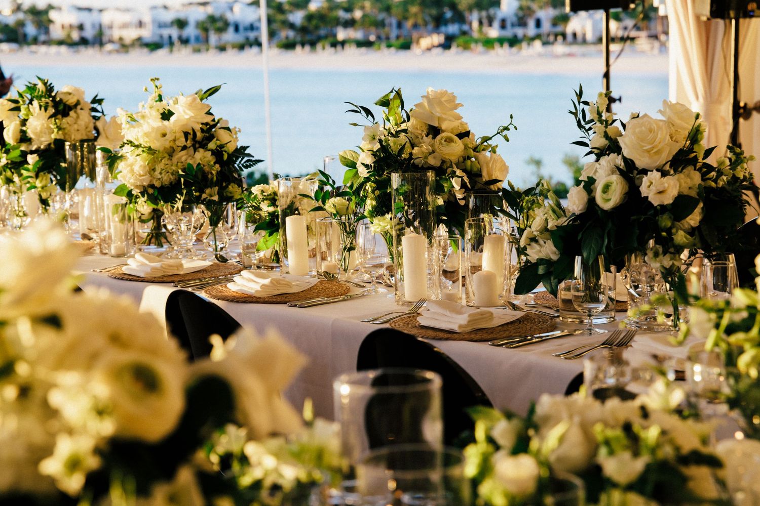 Elegant waterfront wedding reception table with white floral centerpieces and crystal glassware.