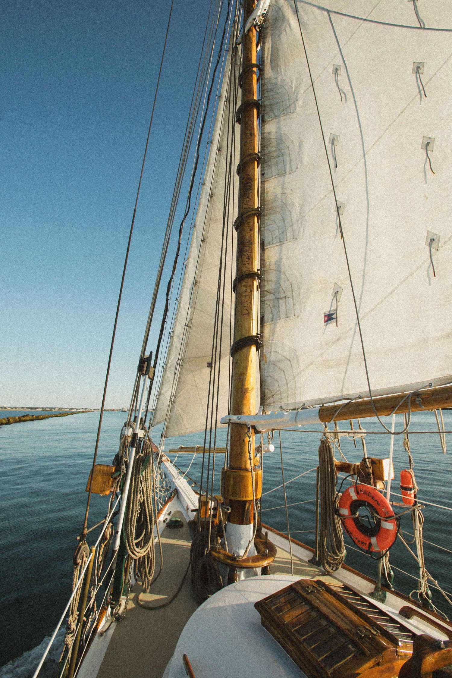 View of white sails and rigging on a traditional wooden sailboat against blue sky.