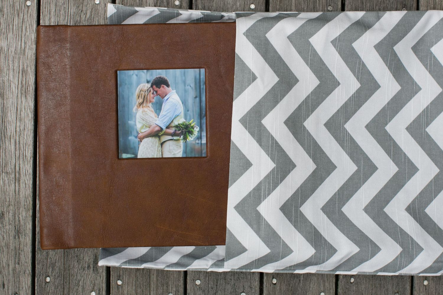 Wedding photo album displayed on weathered wood with chevron pattern and photo frames.