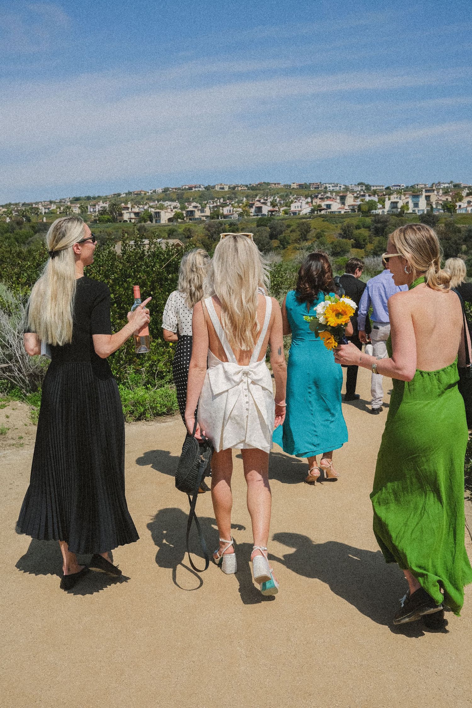 Wedding guests walking along a scenic coastal path with ocean and hillside views.
