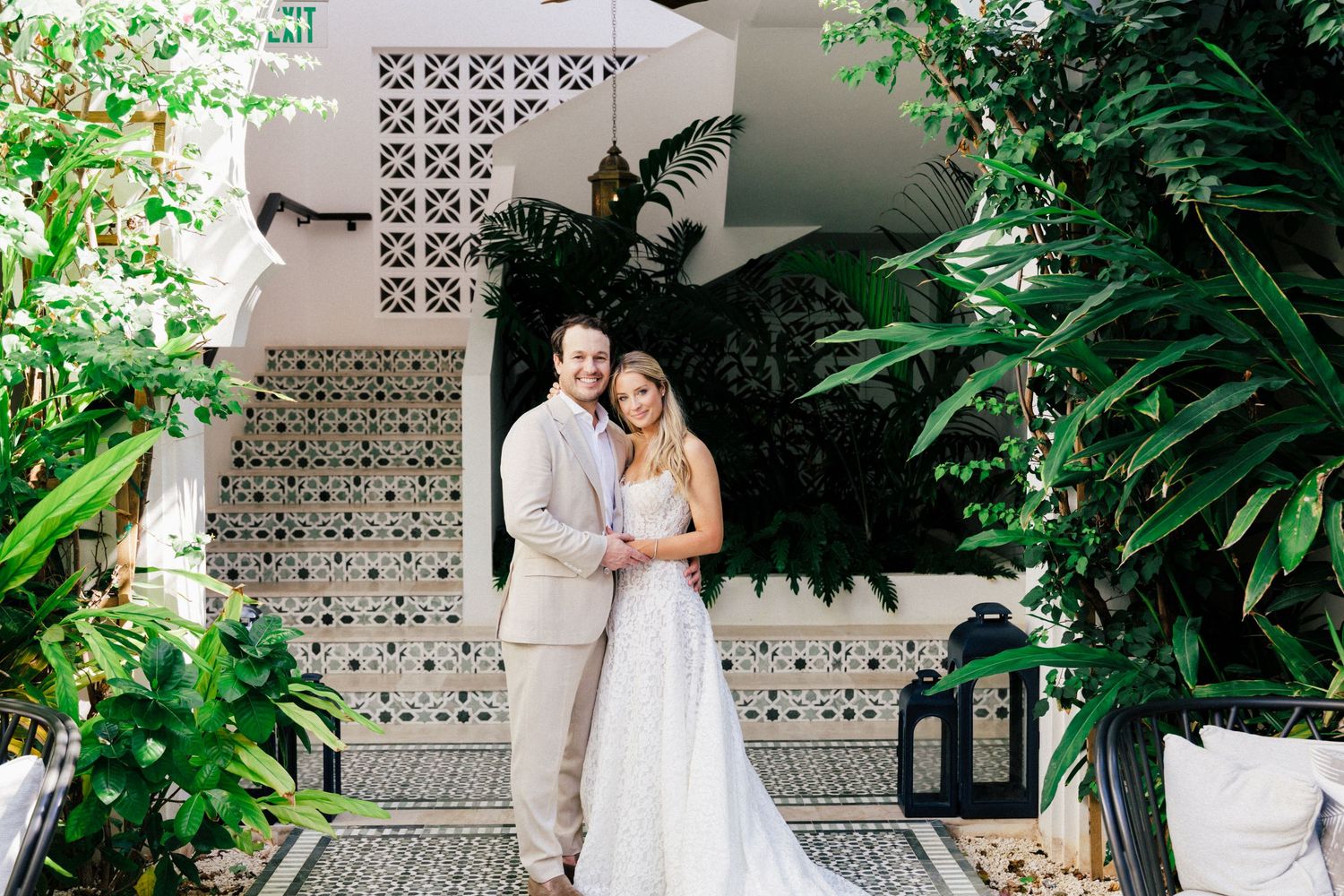 Elegant white wedding ceremony space with tropical greenery and decorative breeze block walls.