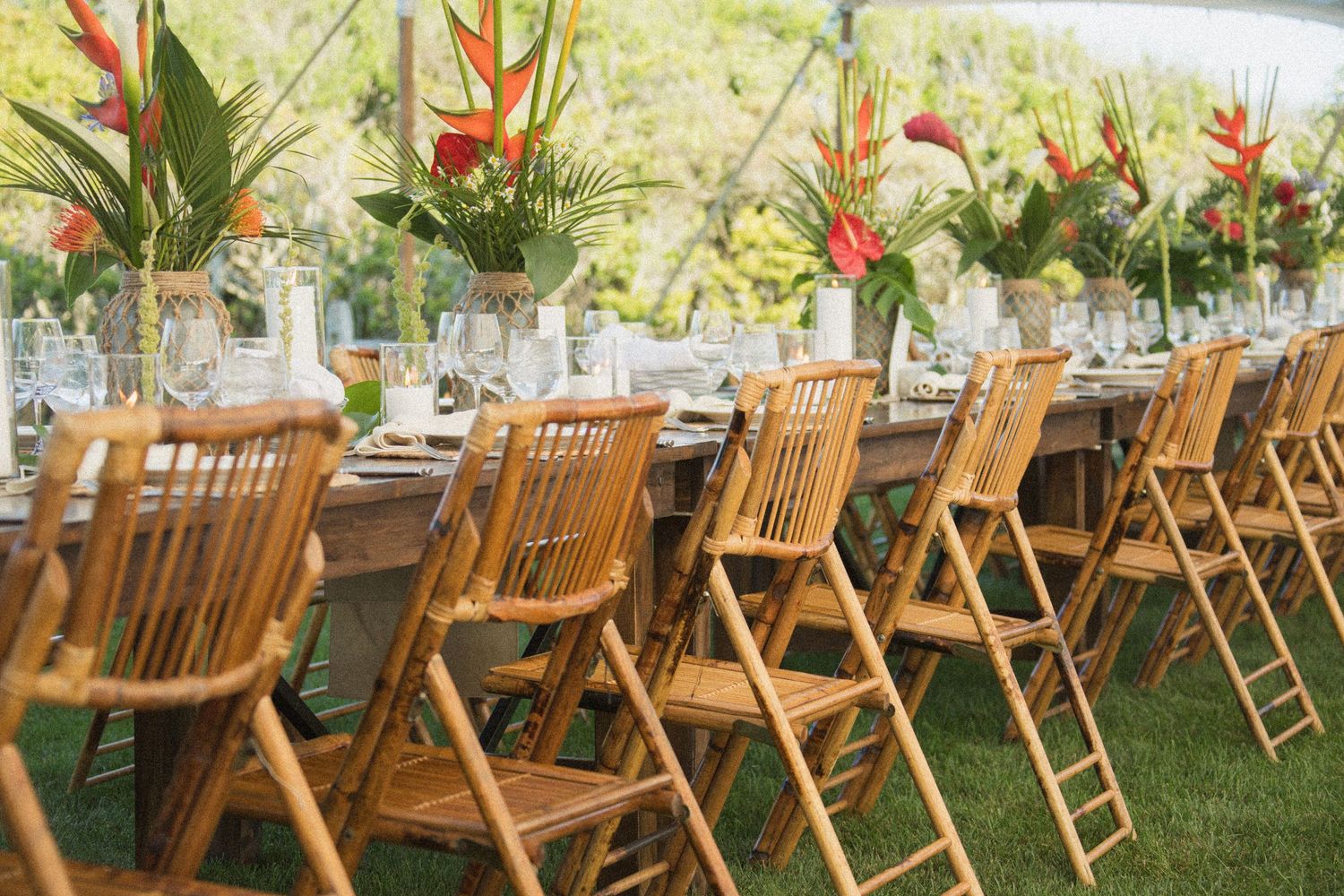 Elegant outdoor wedding reception table setup with wooden chairs and tropical flower centerpieces.