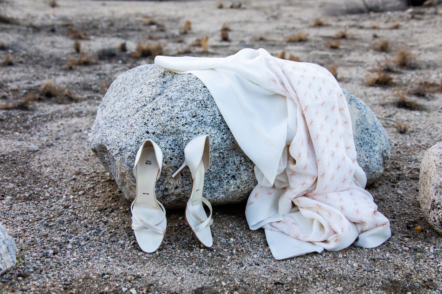 Wedding dress and shoes laid out on desert sand with rocks.
