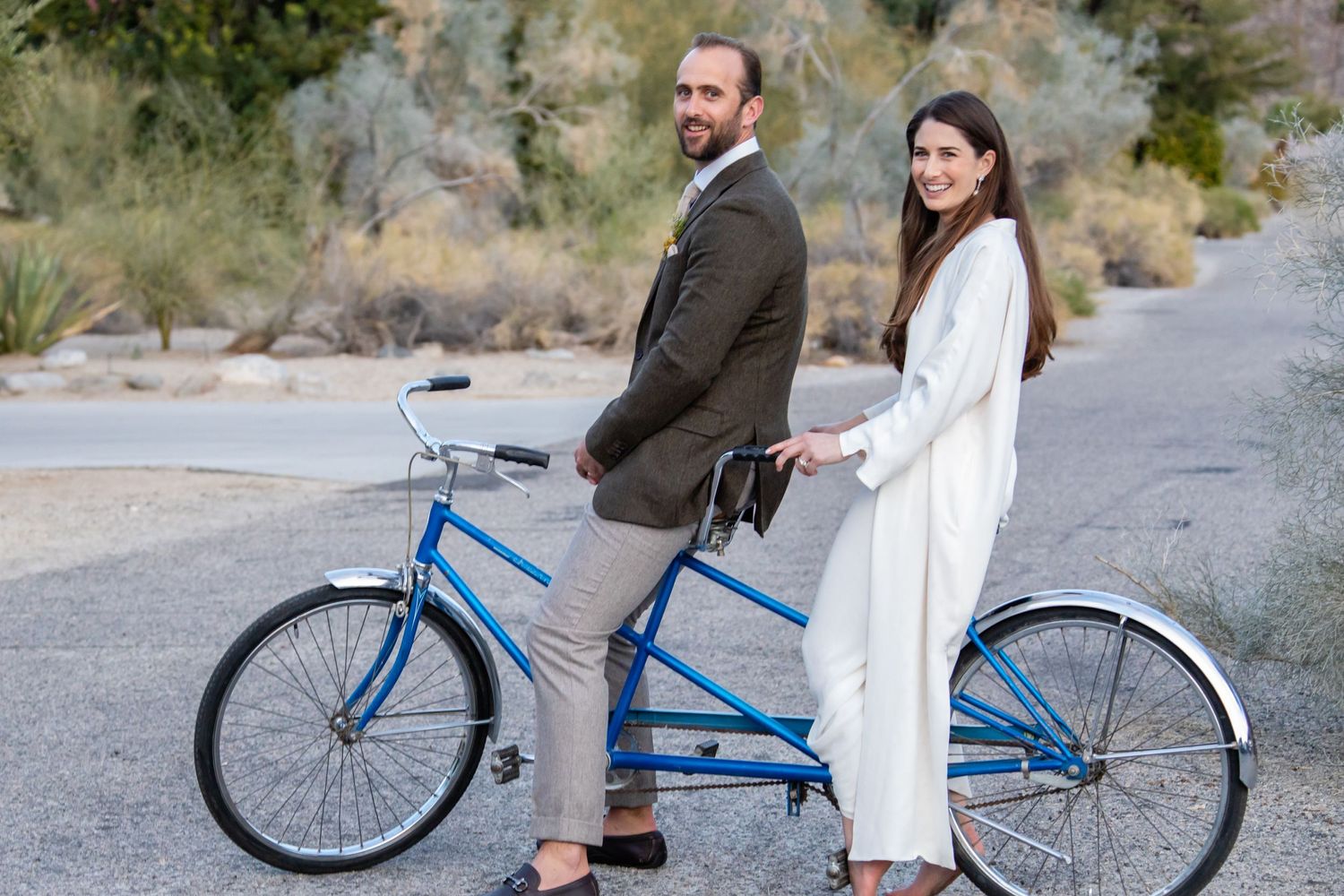A couple shares a blue bicycle ride through a desert landscape with mountains in view.