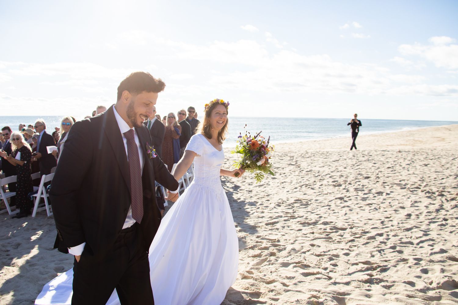 Wedding celebration on a sunny beach with guests watching the happy couple.