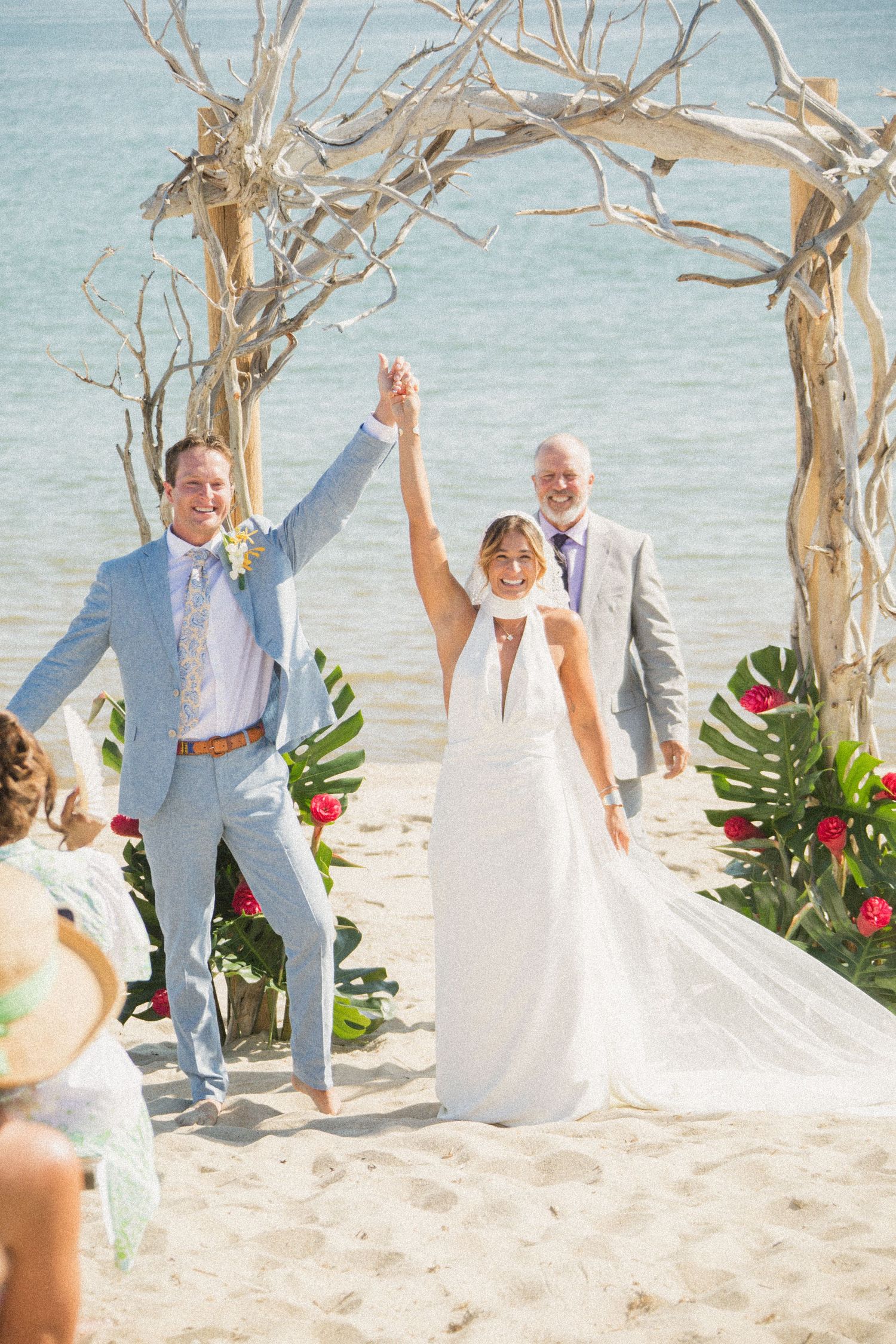 Newlyweds celebrating with raised arms under beach wedding arch.