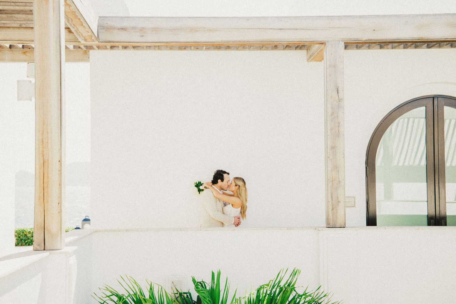 Modern white interior venue space decorated with tropical plants and archways.