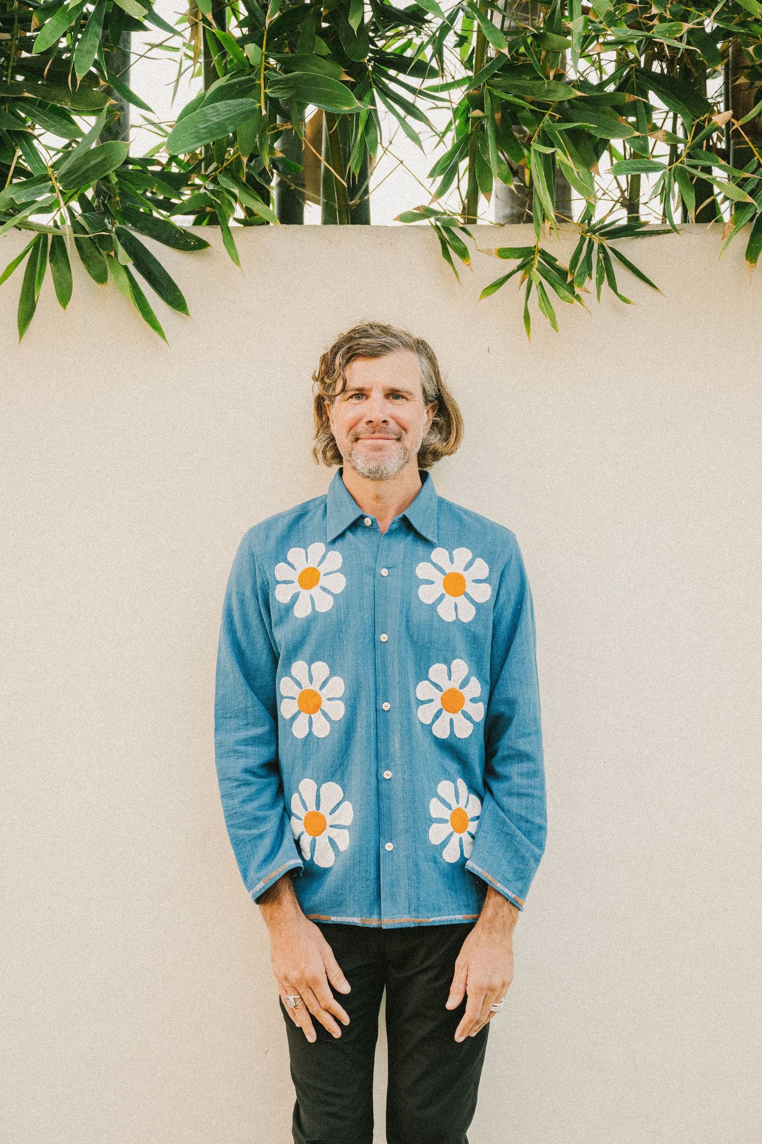 Denim jacket with decorative white daisy patches against white wall with green plants.
