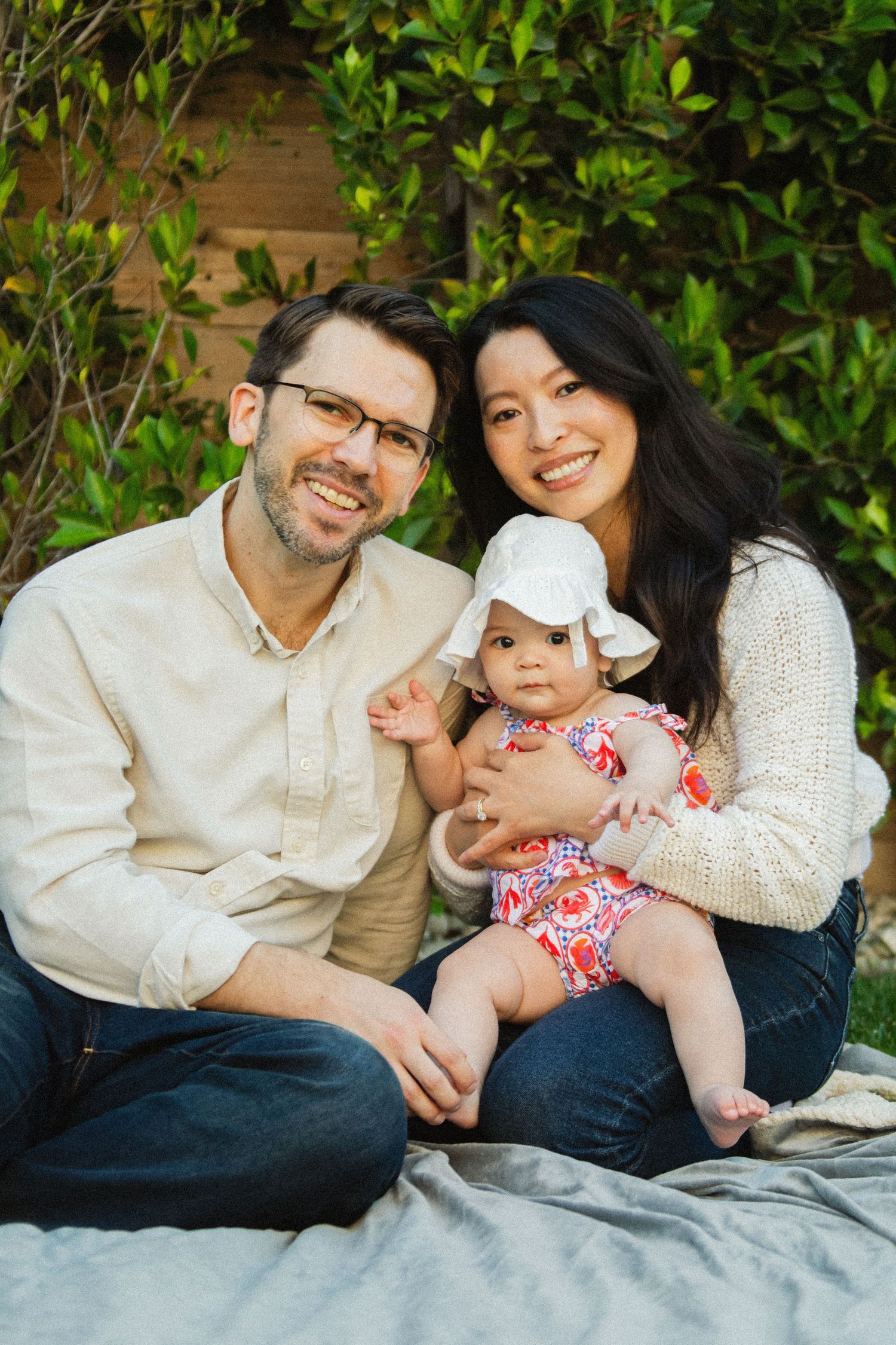 Family relaxing together on a blanket against a lush green garden backdrop.