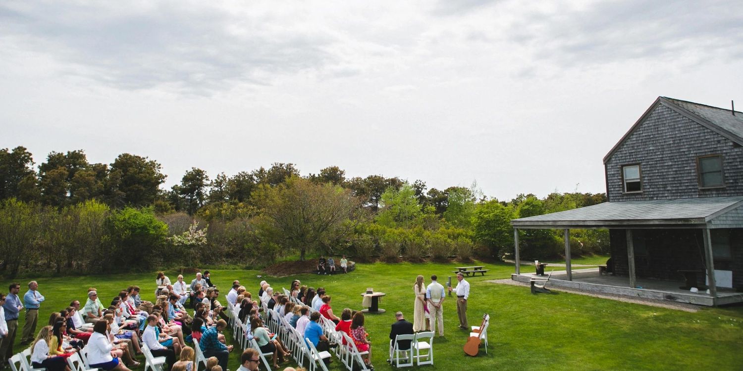 Panoramic view of an outdoor wedding ceremony setup with guests seated on a grassy hillside.