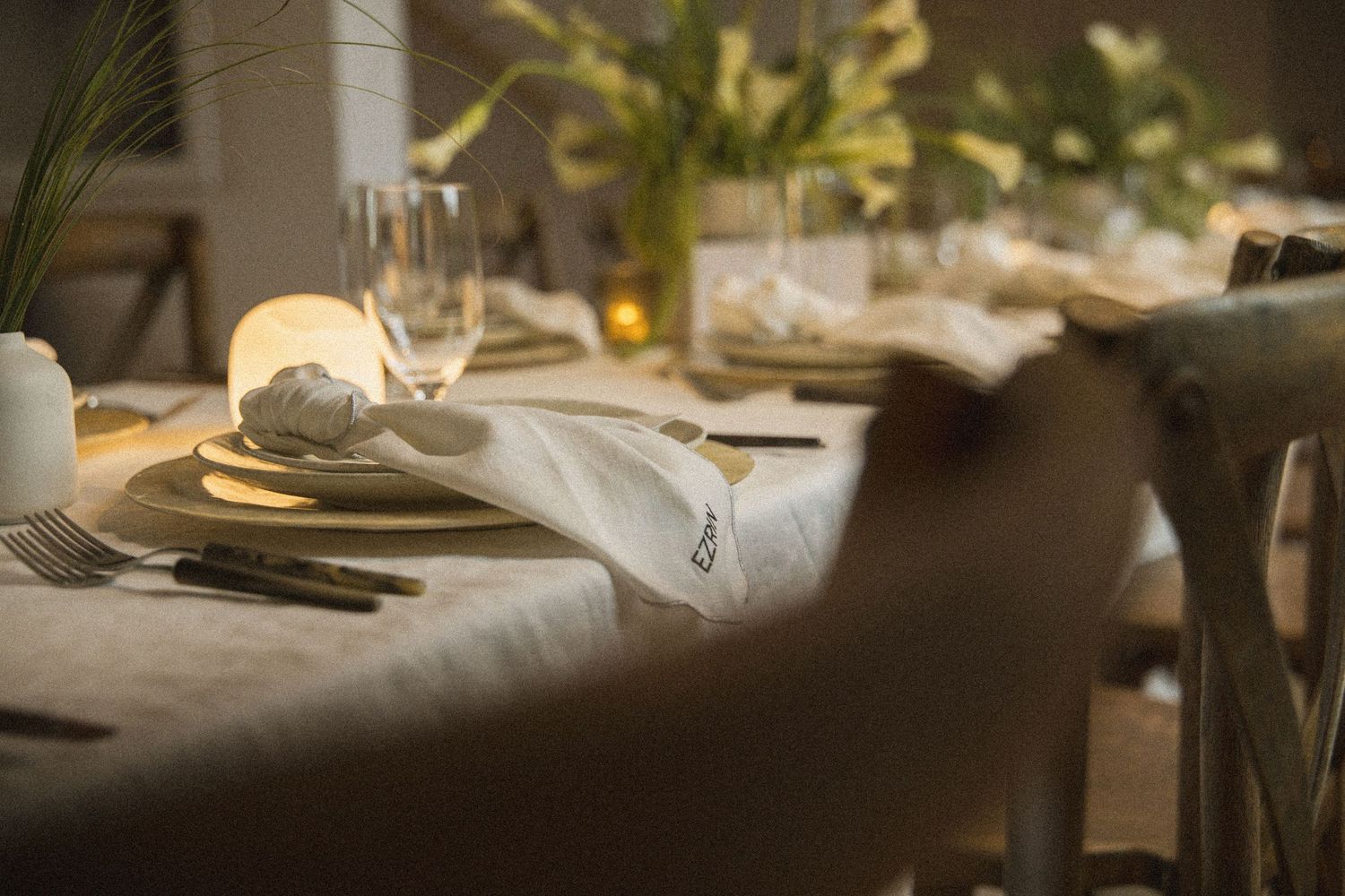 Elegant dinner table setting with gold plates, folded napkins, glassware, and soft candlelight in a warm dining room.