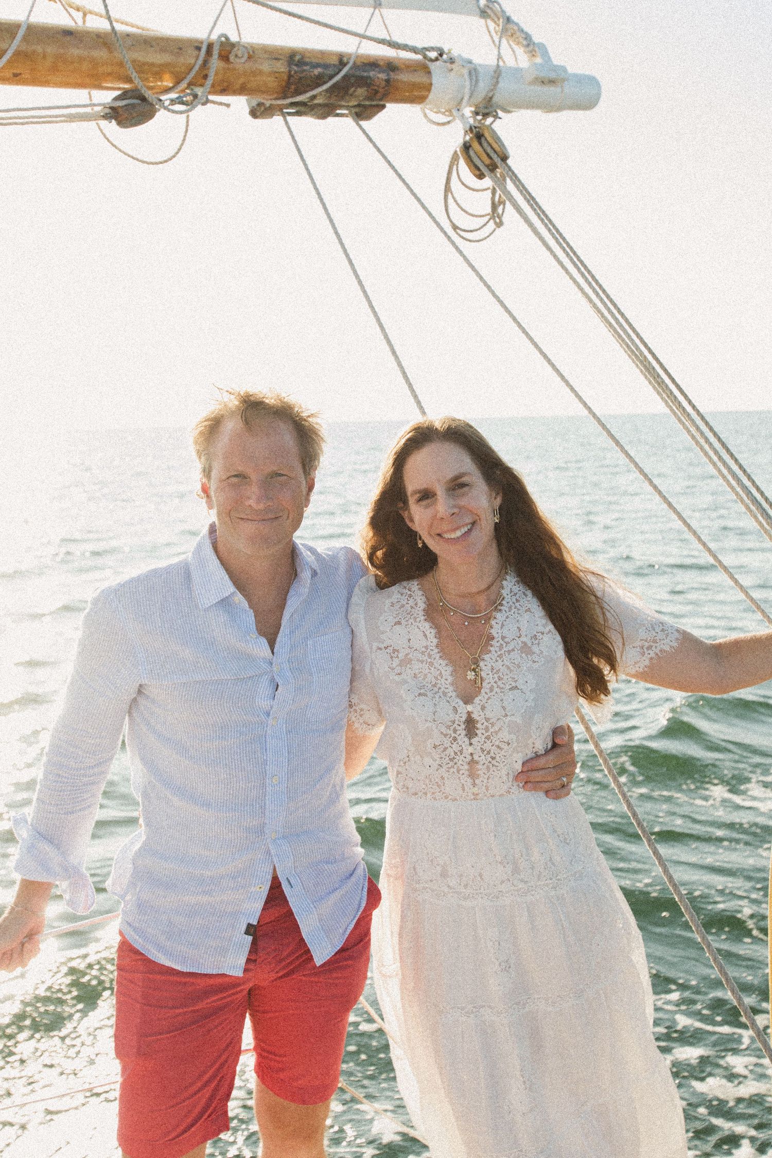 Couple dressed in white and red outfits sharing a romantic moment on a sailboat deck.