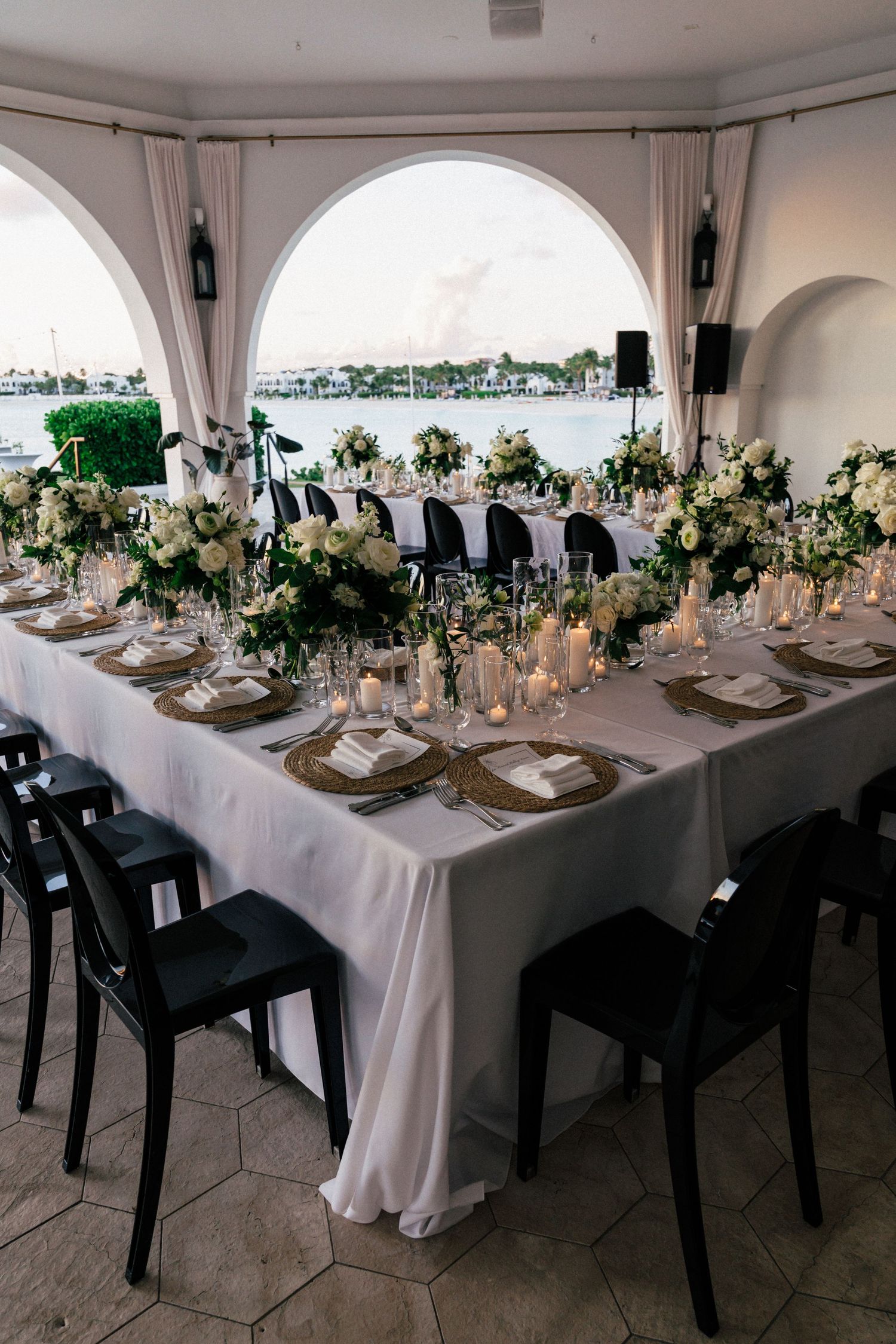 Luxurious wedding reception table with white and green florals under arched waterfront venue.
