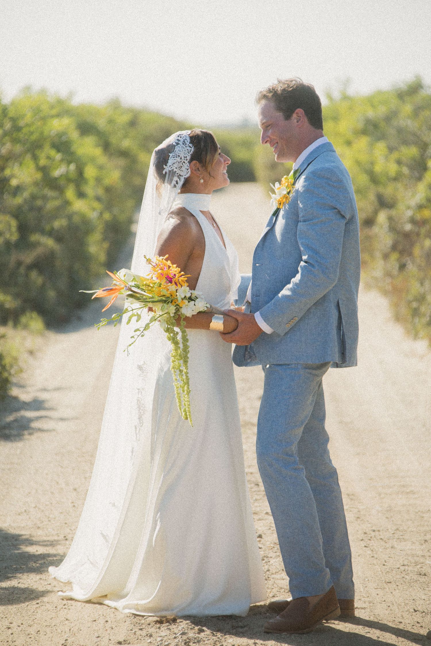 Newlyweds share a tender moment on a scenic path with the bride holding a vibrant tropical bouquet.