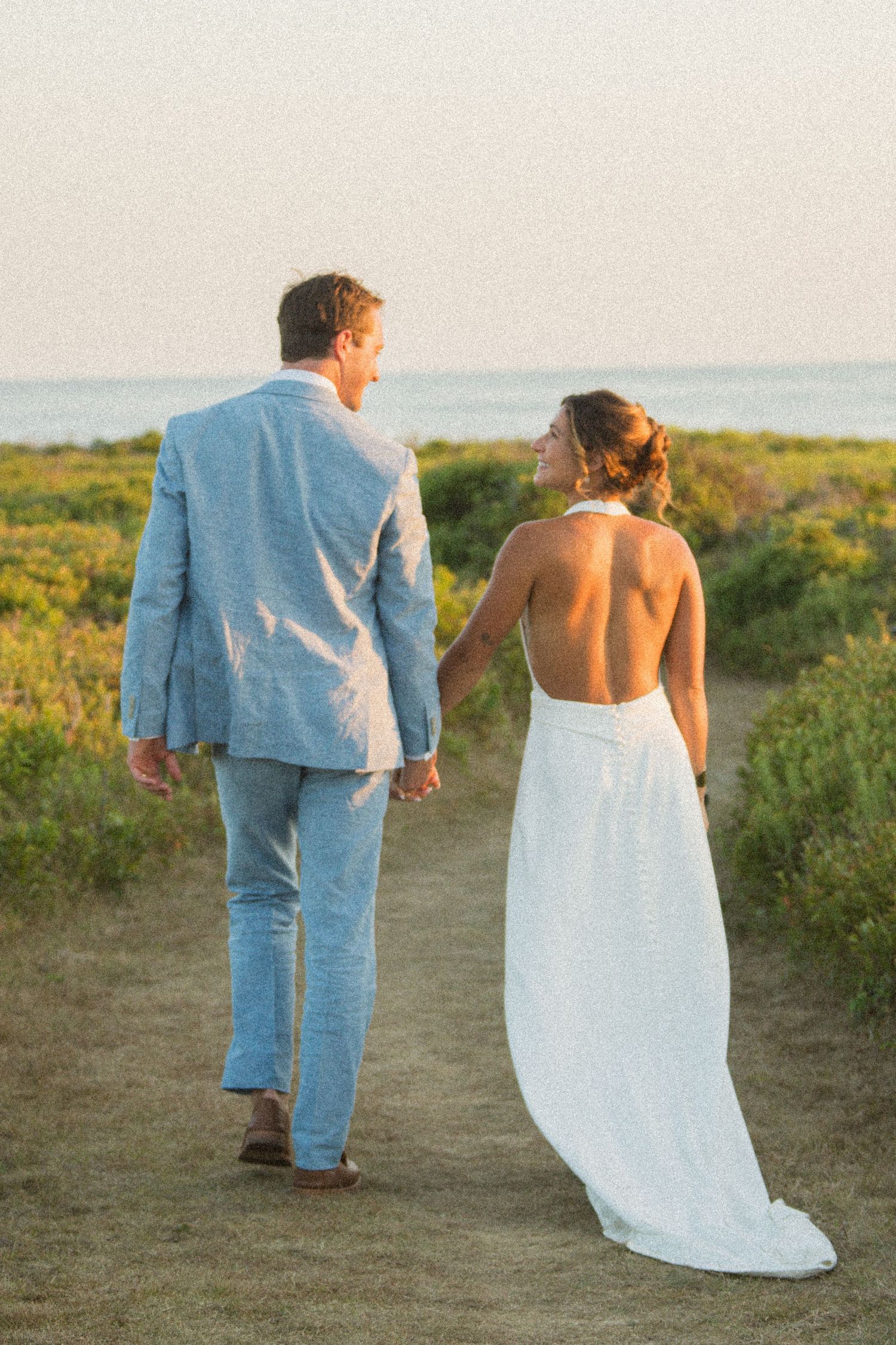 Couple walks along a coastal path at sunset after their wedding ceremony.