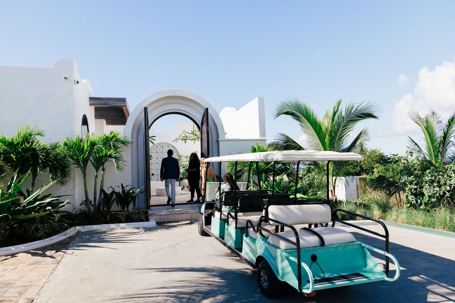 Turquoise golf cart parked under archway at tropical resort entrance.