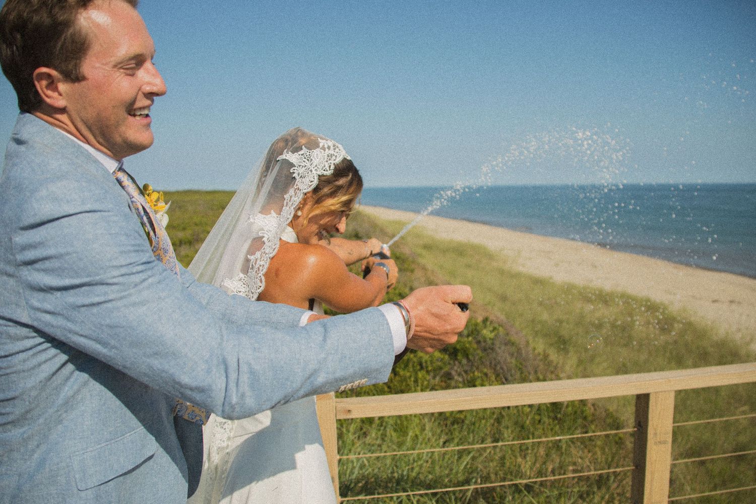 Champagne celebration on coastal boardwalk with ocean view and beach grass.