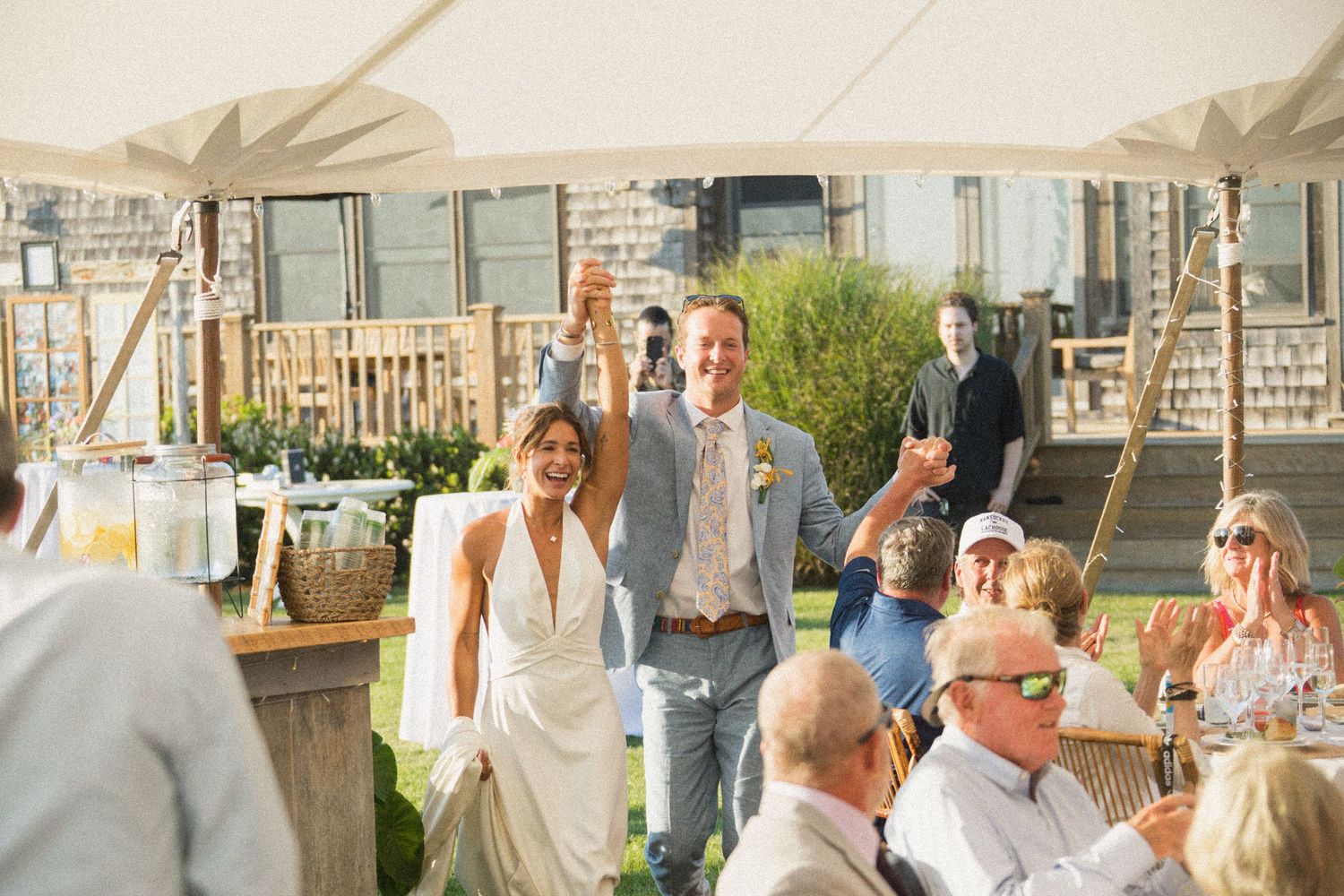 Guests mingling under white tent at outdoor reception.