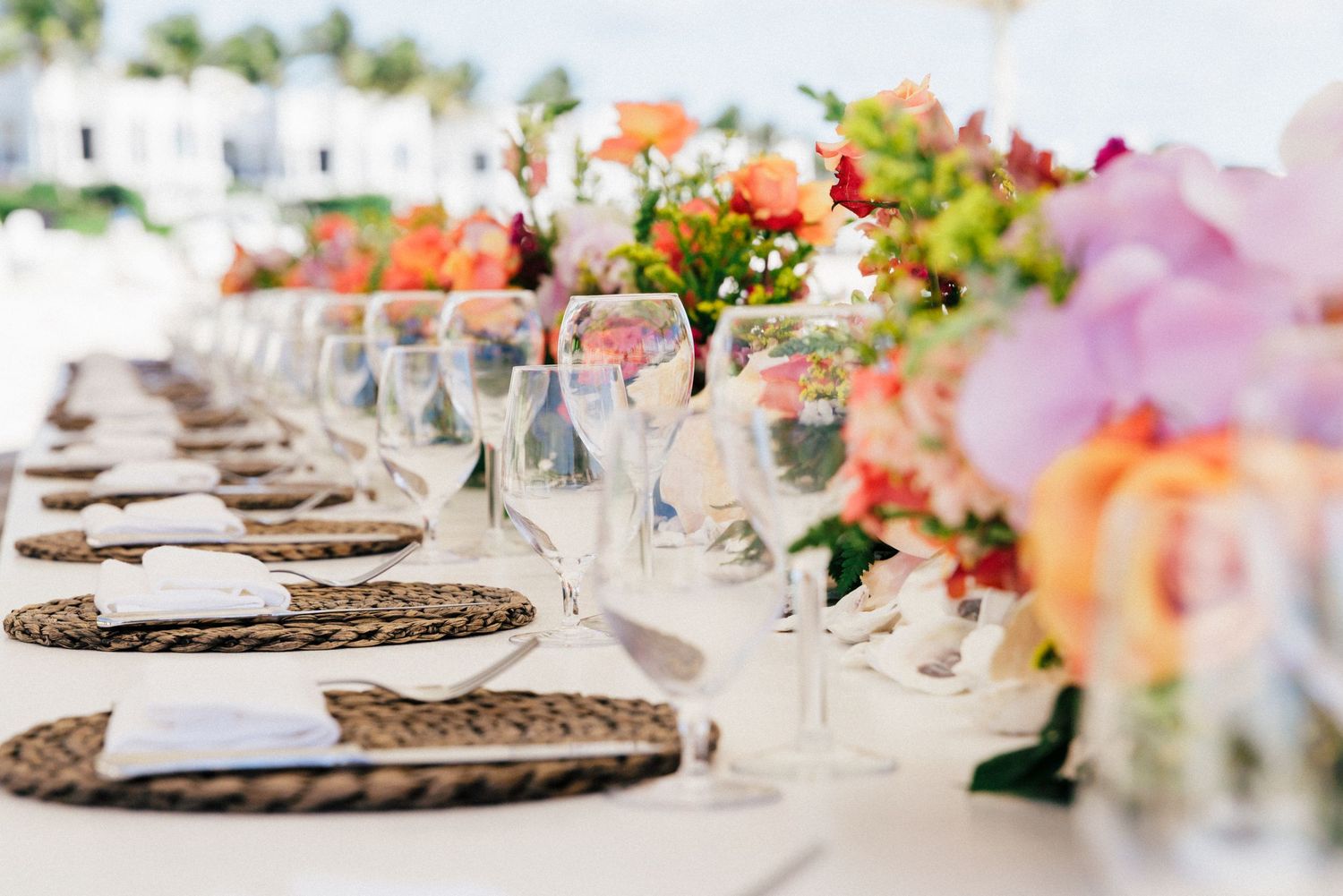 Elegant table settings with coral and peach floral arrangements at a beachside wedding.