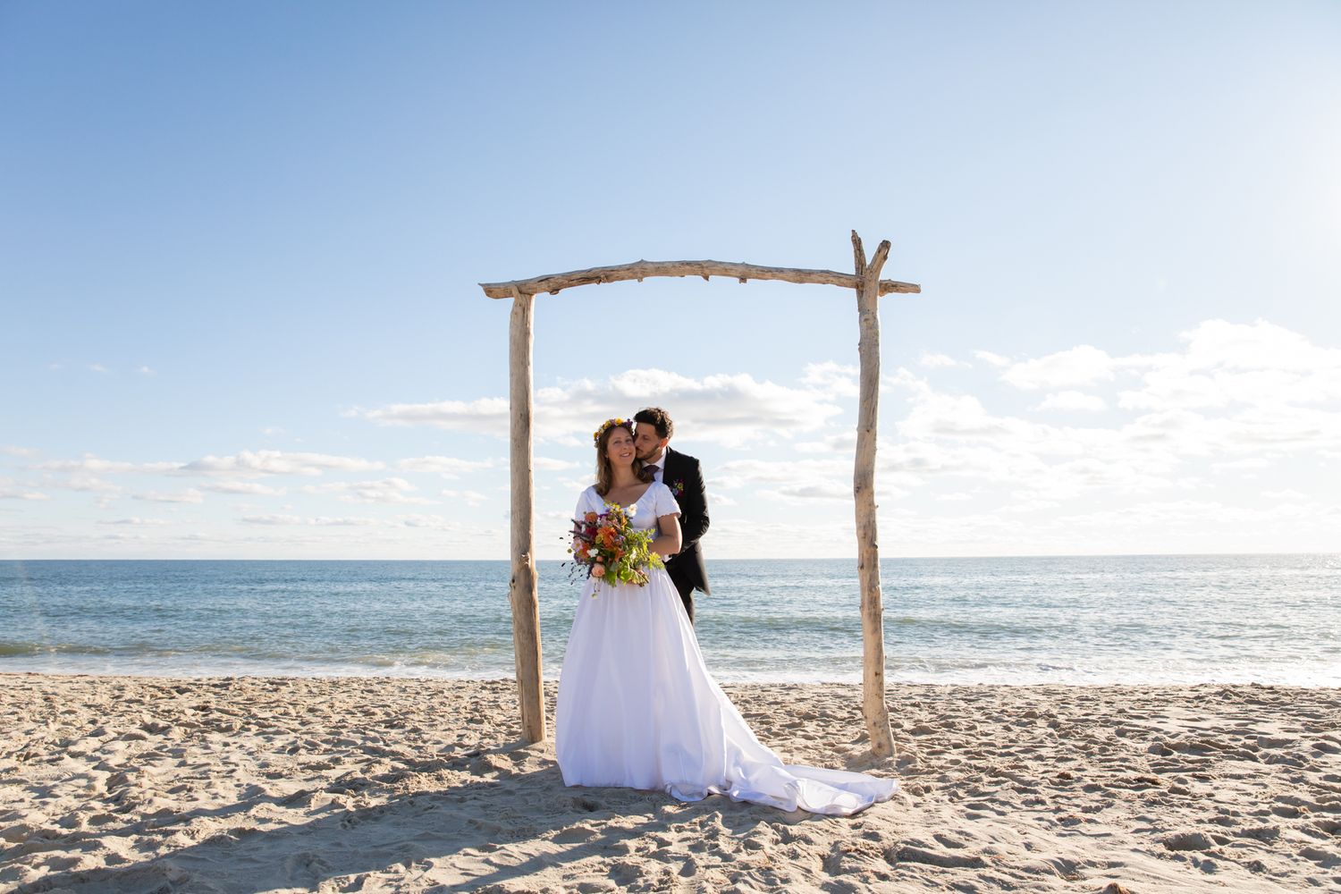 Minimalist beach wedding setup with driftwood arch against ocean waves.