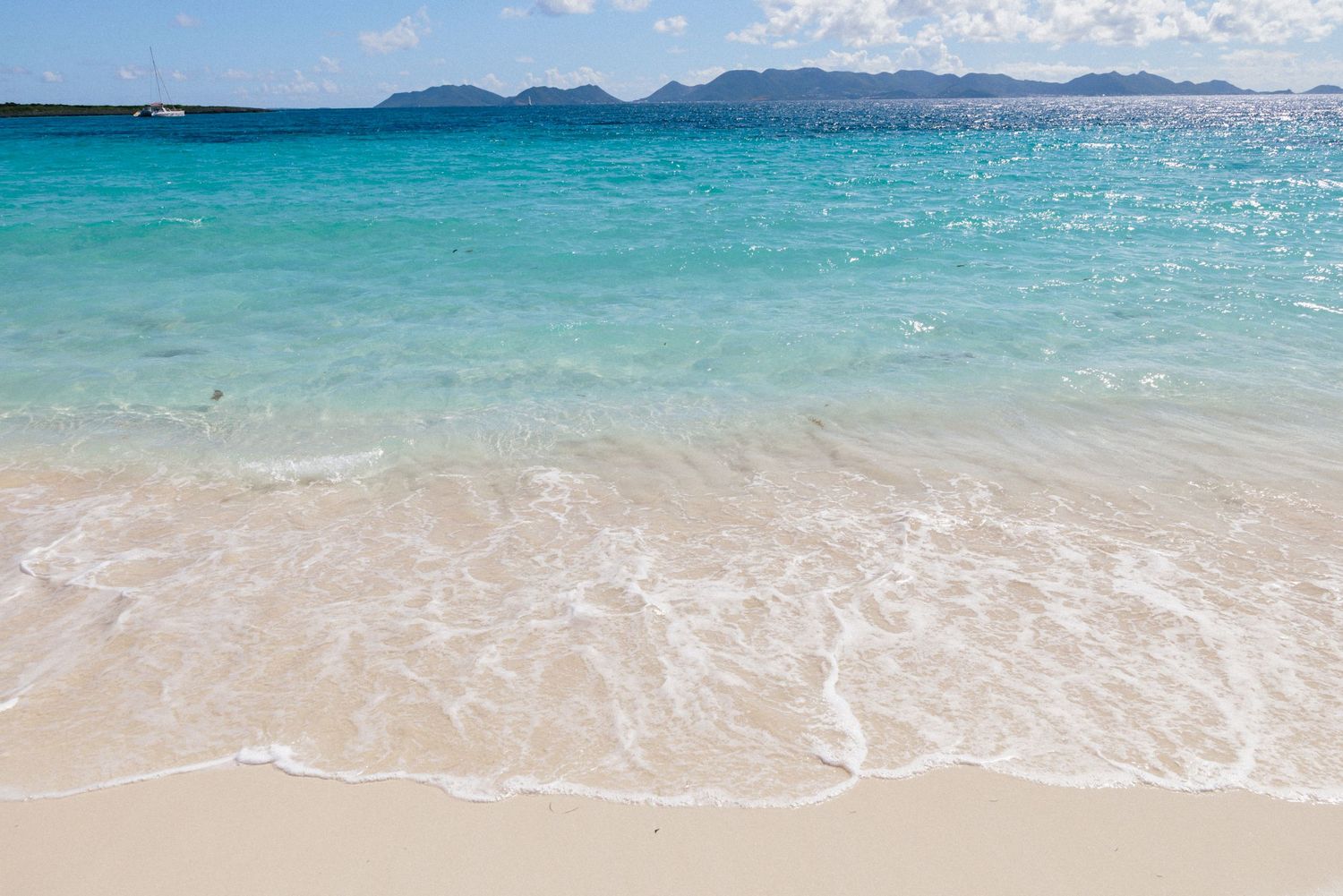 Pristine turquoise ocean waters meeting white sandy beach under blue sky.