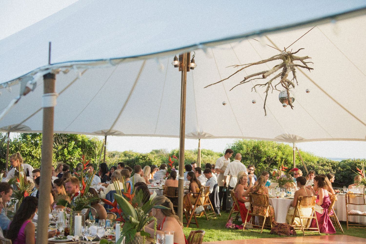 Wedding reception under white tent with hanging decorations and crowd of guests.