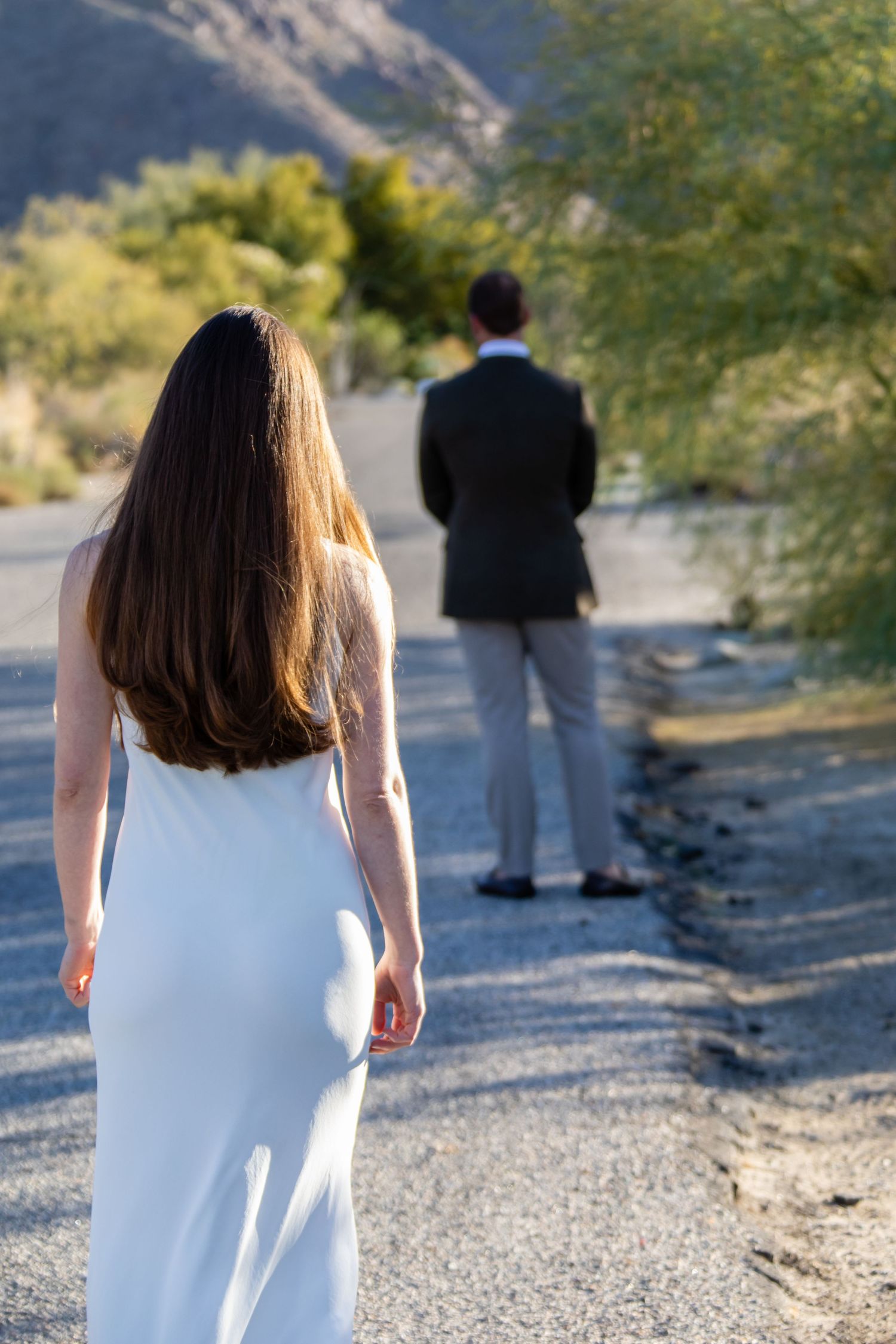 Two people in formal attire standing on a desert path.