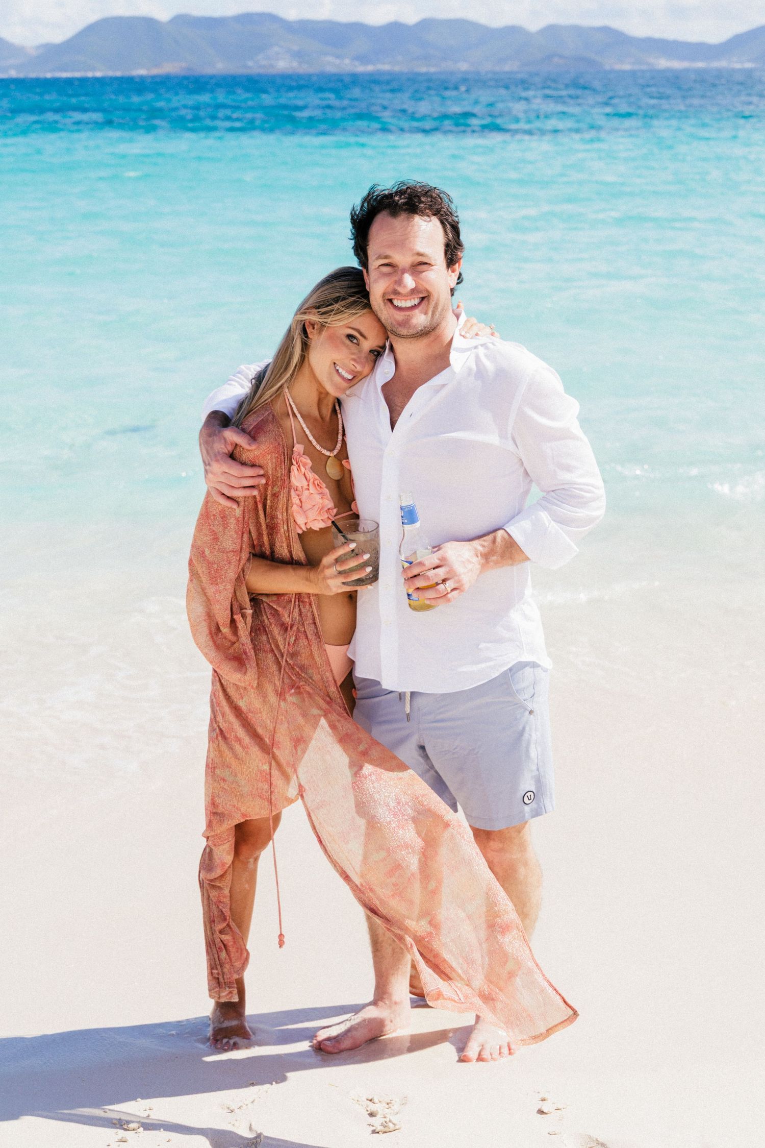 Couple sharing a romantic moment on a pristine beach with mountains in the background.