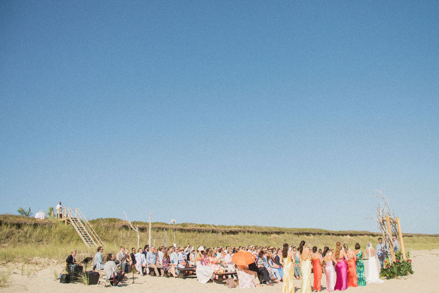Wedding guests seated on the beach with clear blue sky overhead.